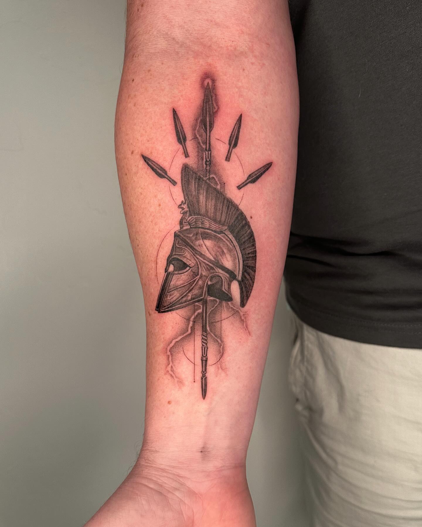 Spartan helmet black and grey tattoo on the forearm by Paige Jean