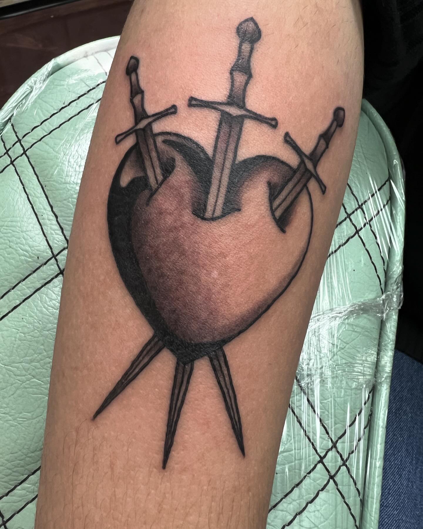 Heart with swords black and grey tattoo on the forearm by Cody Marl