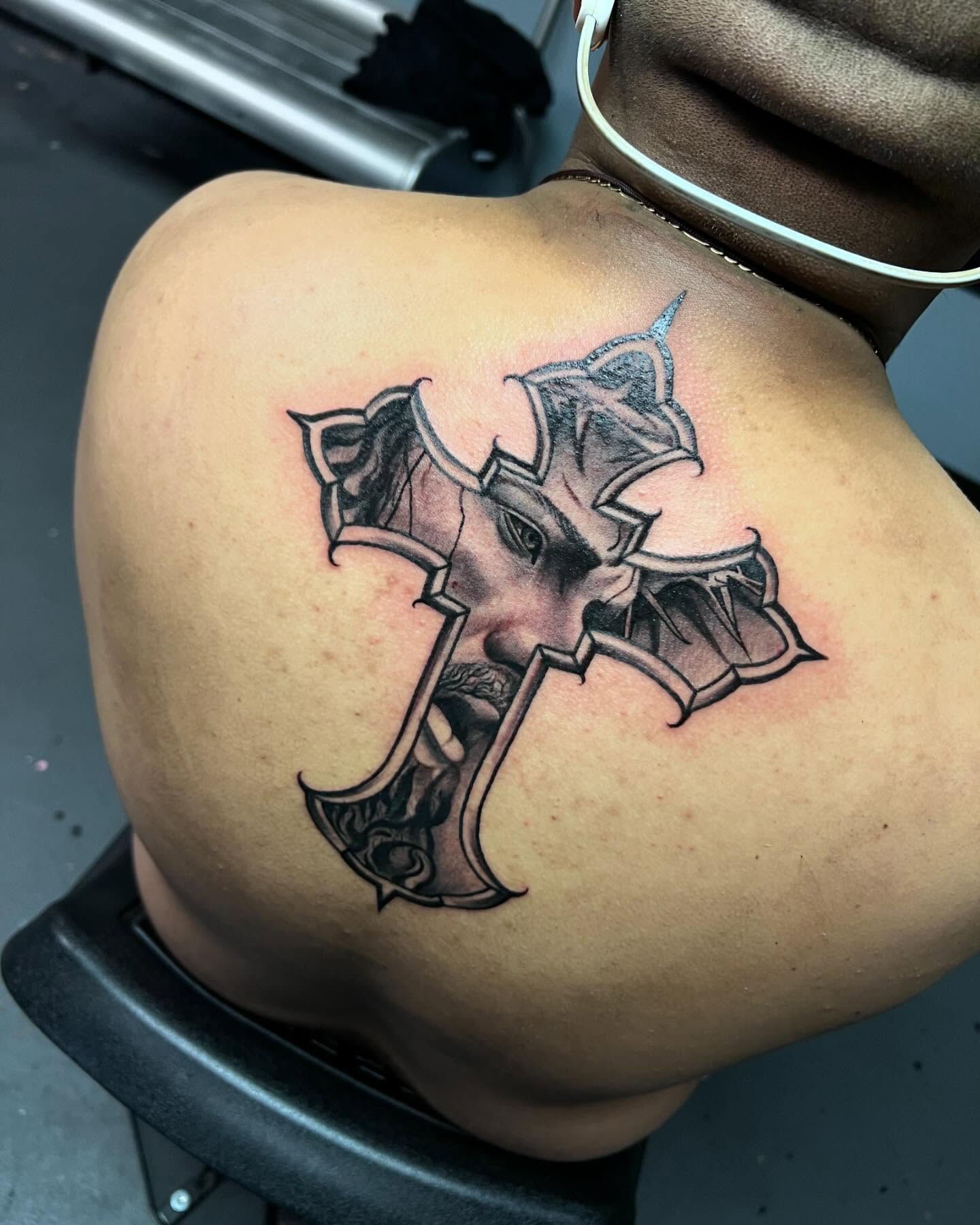 Cross with face black and grey tattoo on the shoulder by Smuk One