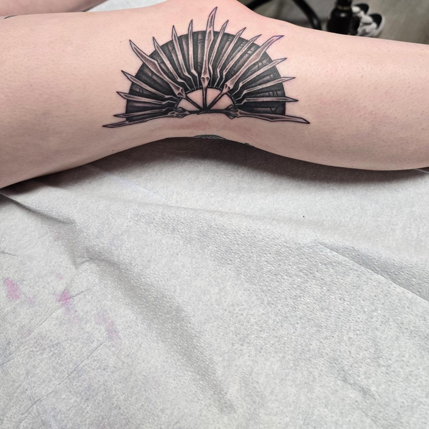 Sunburst with blades black and grey tattoo on the forearm by Gene Britton