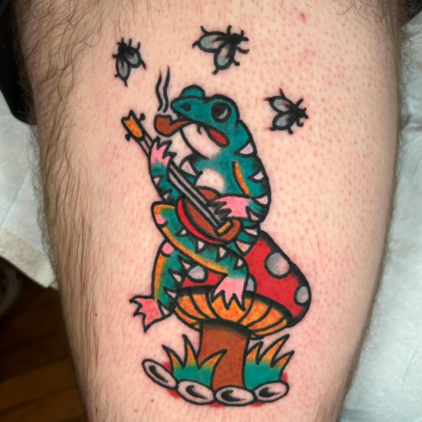 Frog playing guitar American traditional tattoo on the thigh by Emmy Gallagher