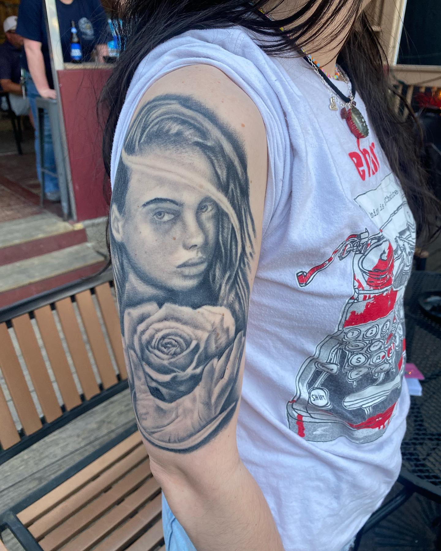 Woman with rose realism tattoo on the upper arm by Brandon Anderson