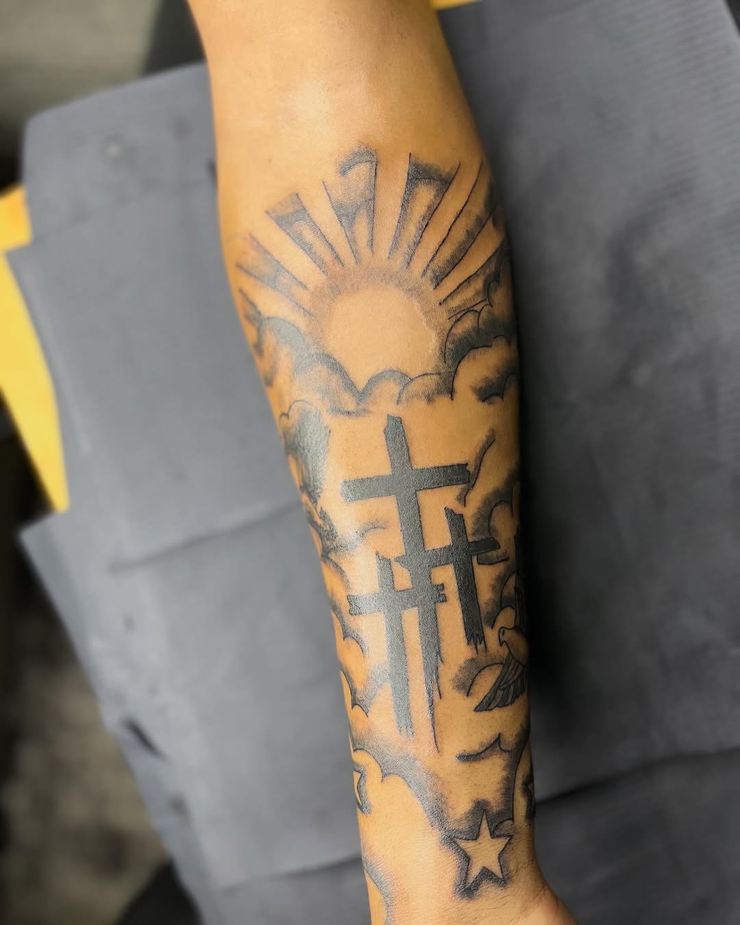 Sun, clouds, crosses, dove, and star Chicano tattoo on the forearm by CmoreInk