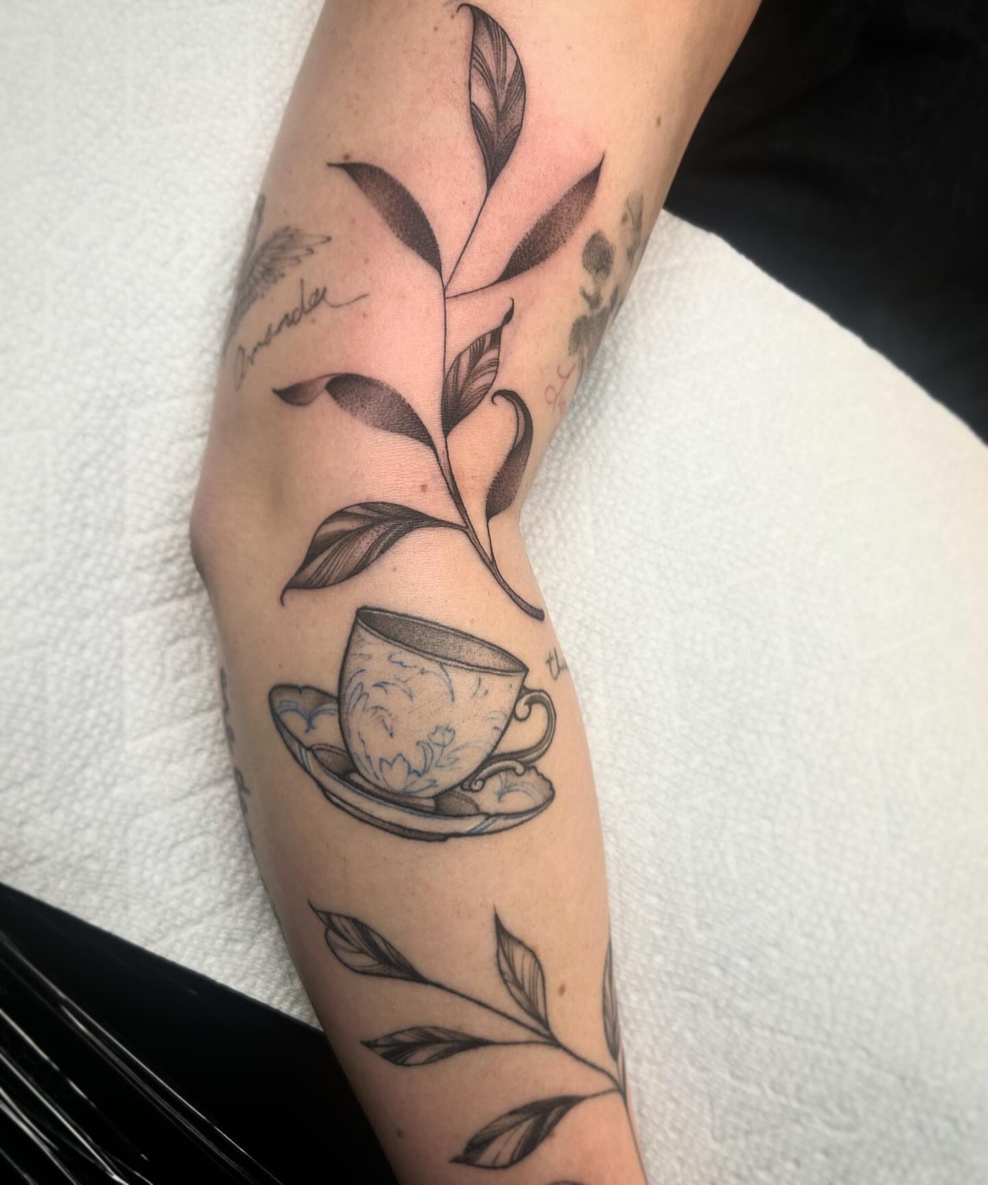 Teacup and leaves black and grey tattoo on the forearm by Lena Lawrence
