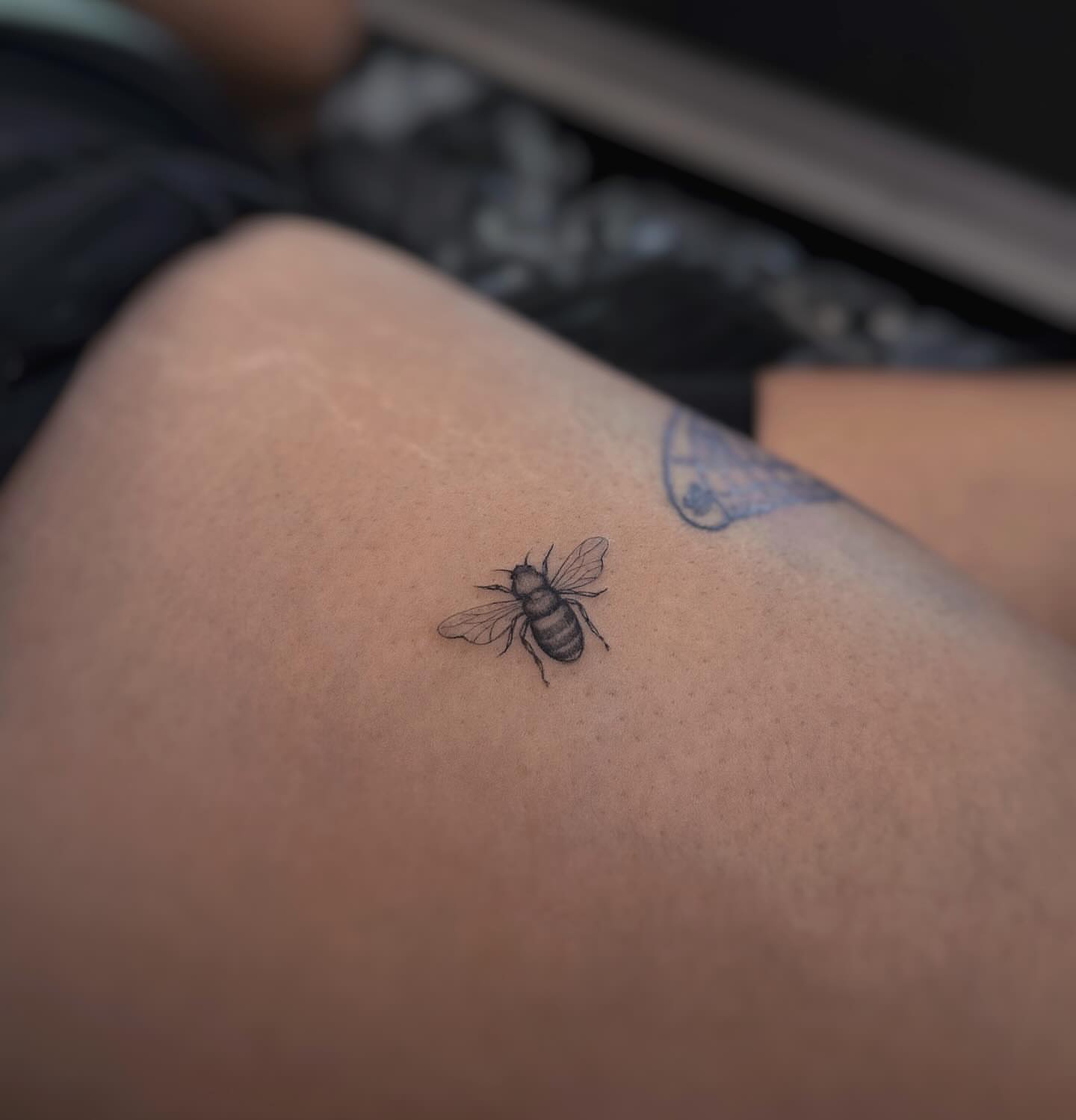 Bee black and grey tattoo on the thigh by Lily K.