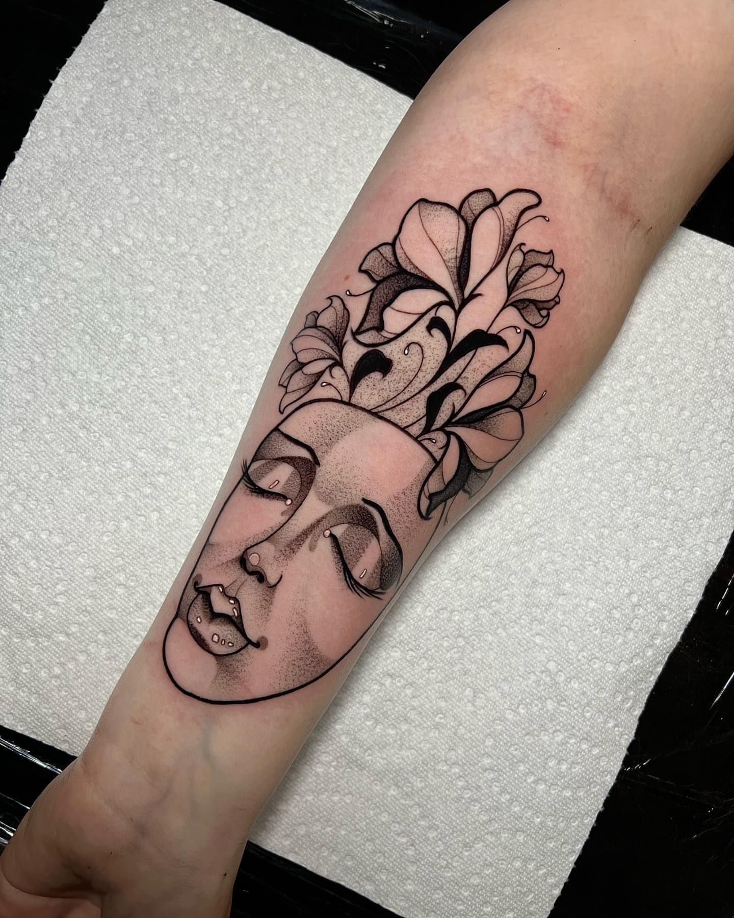 Woman's face with flowers dotwork tattoo on the forearm by Bell Bolton