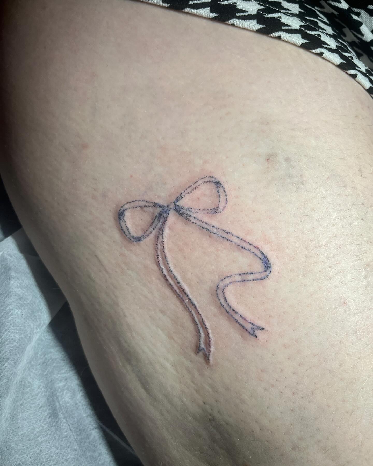 Bow minimalist tattoo on the thigh by hana