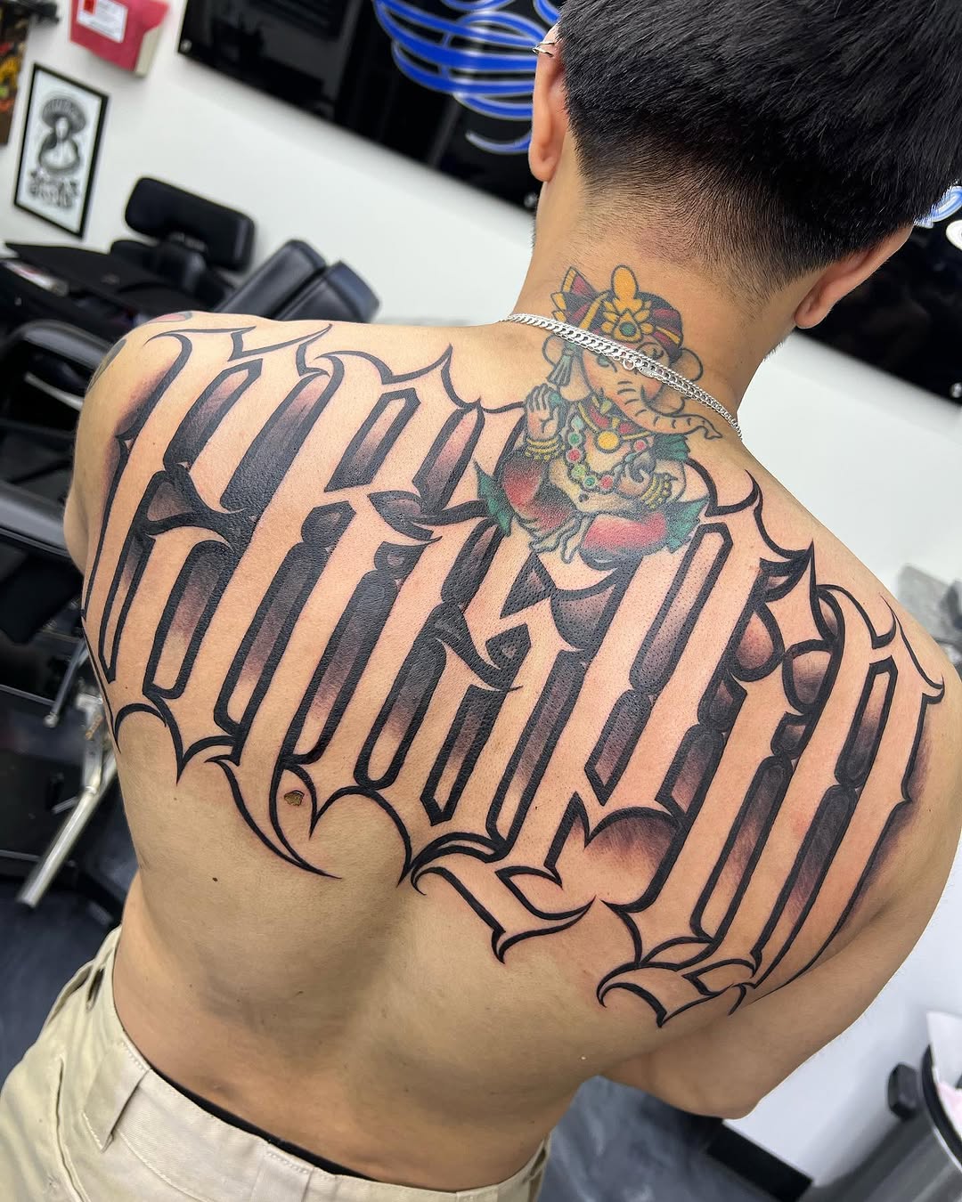 Ganesha and script lettering Chicano tattoo on the back by 𝕾𝖈𝖗𝖎𝖕𝖙 𝕾𝖕𝖊𝖈𝖎𝖆𝖑𝖎𝖘𝖙