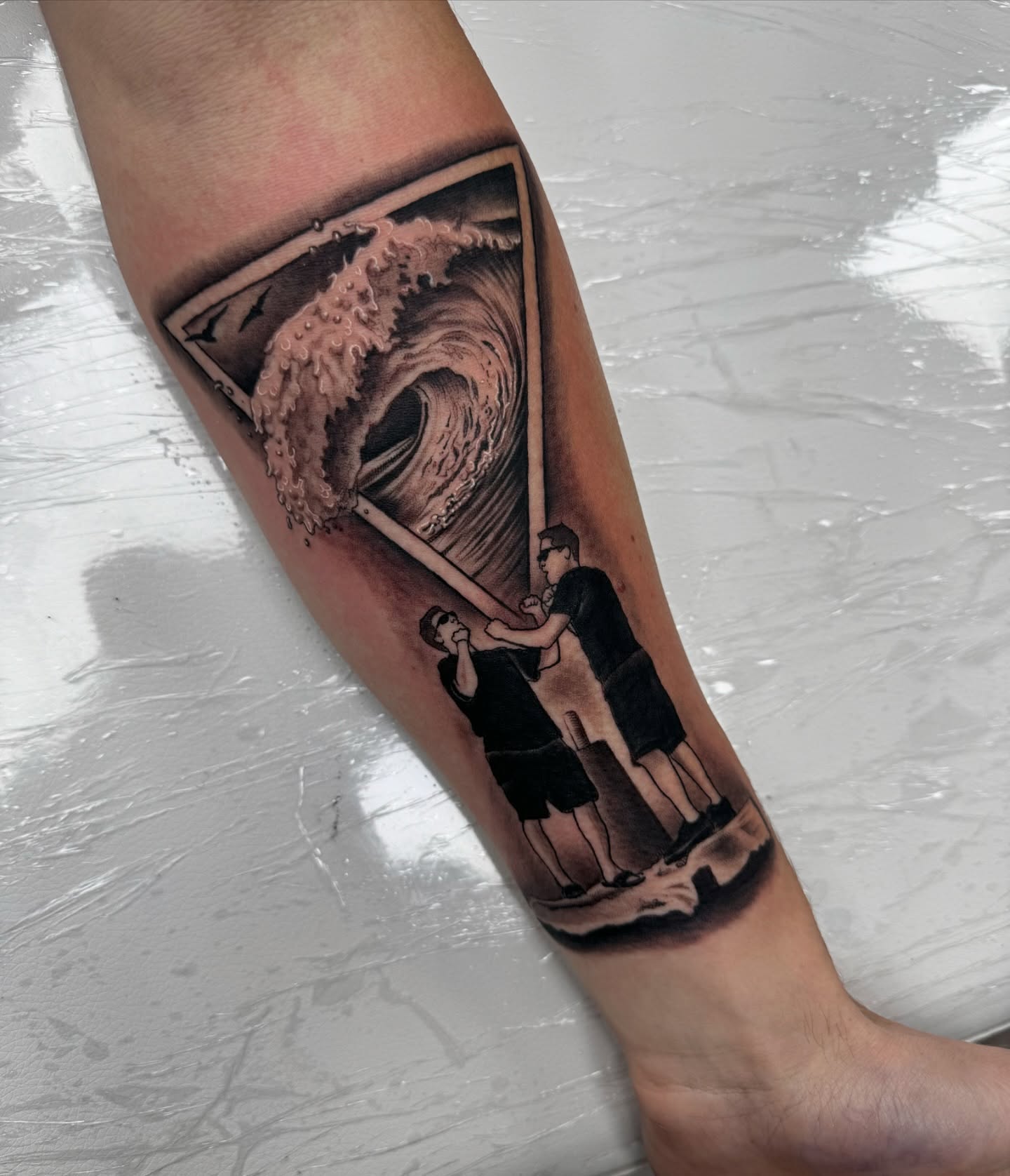 Wave and figures realism tattoo on the forearm by Mike Hudson