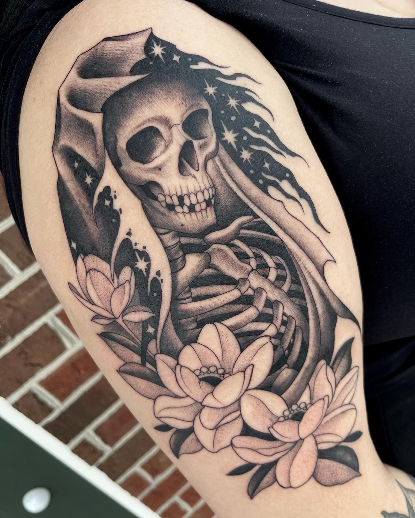 Skull and flowers realism tattoo on the upper arm by Kelsi Steffensen