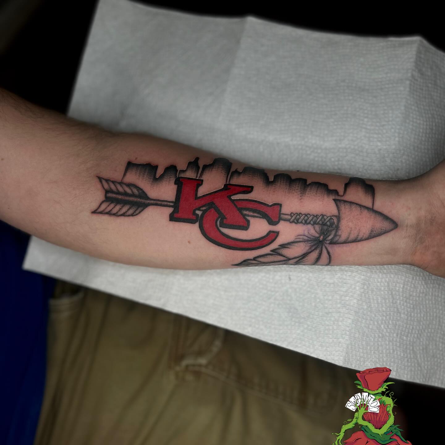 Kc logo with arrow American traditional tattoo on the forearm by Marques Neal
