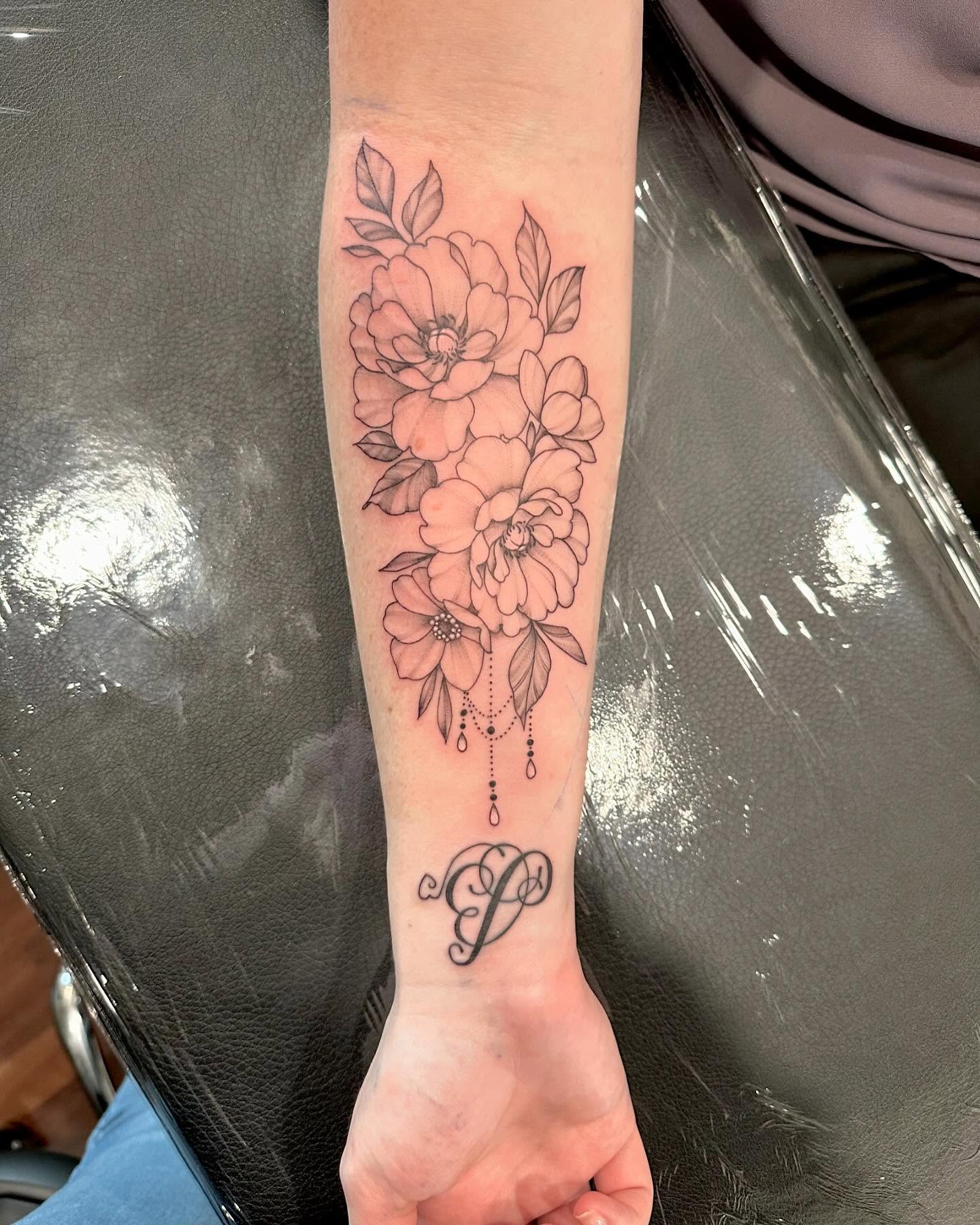 Flowers and monogram black and grey tattoo on the forearm by Kate Darling