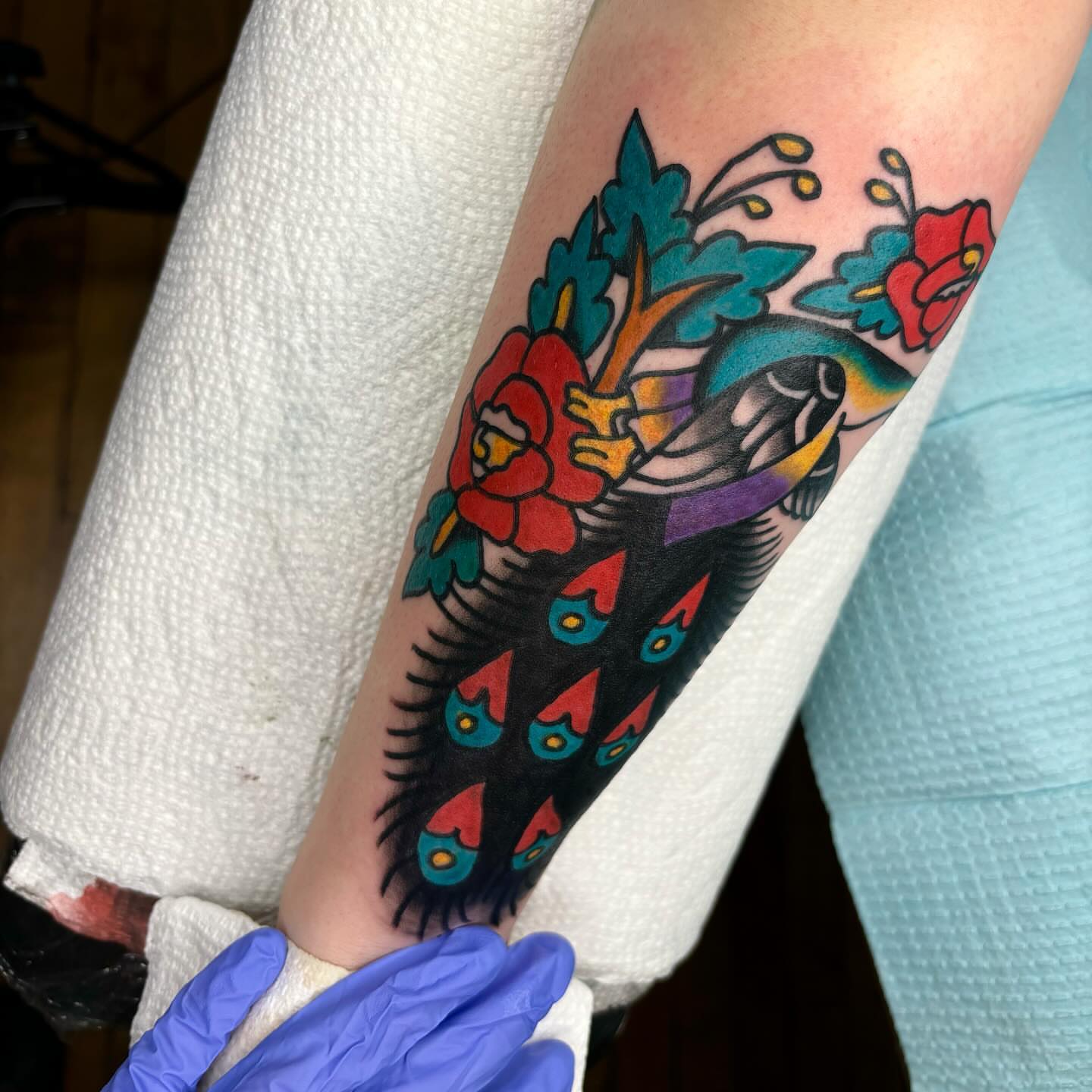 Peacock feathers and flowers American traditional tattoo on the forearm by Emmy Gallagher