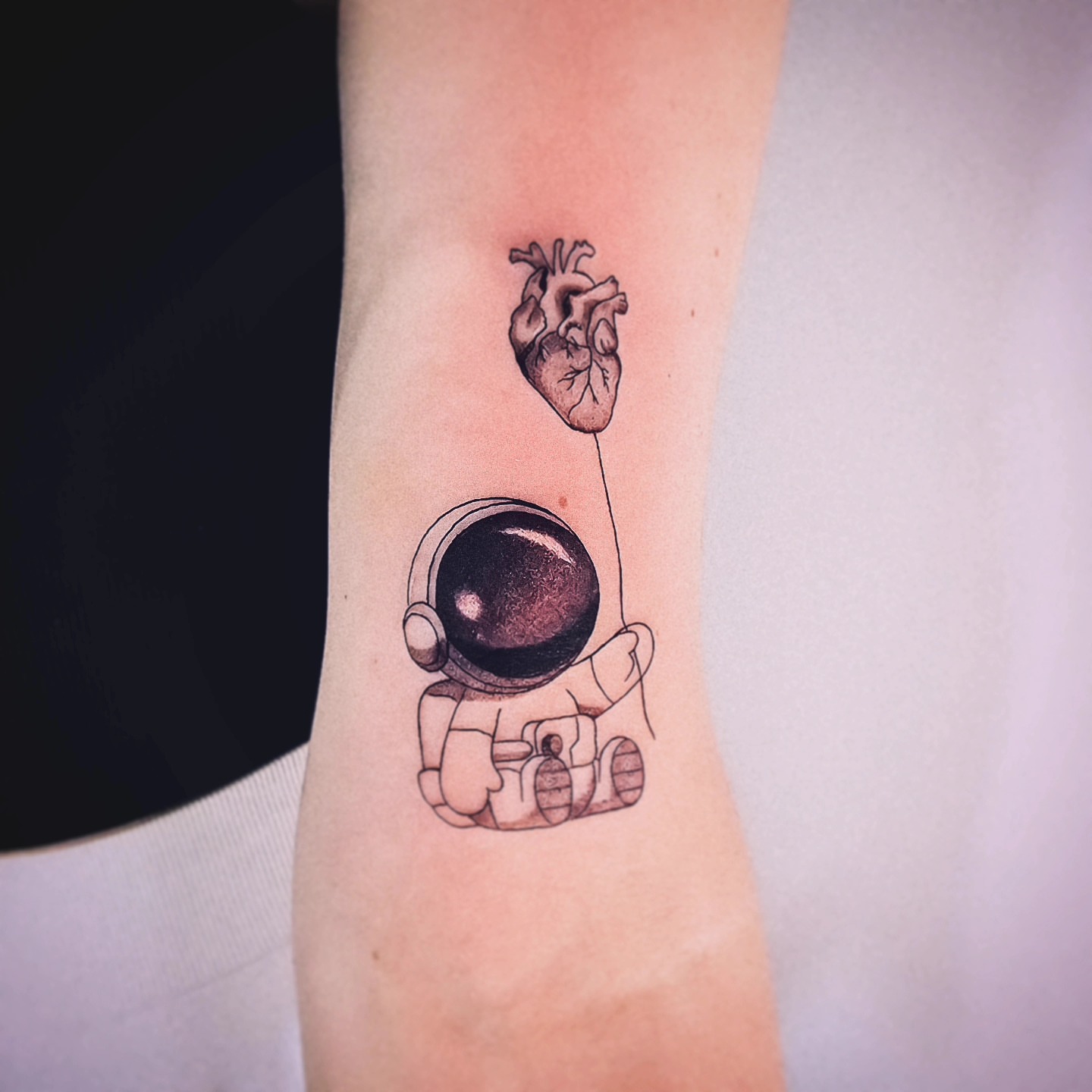 Astronaut holding heart realism tattoo on the forearm by Johnathan Nguyen