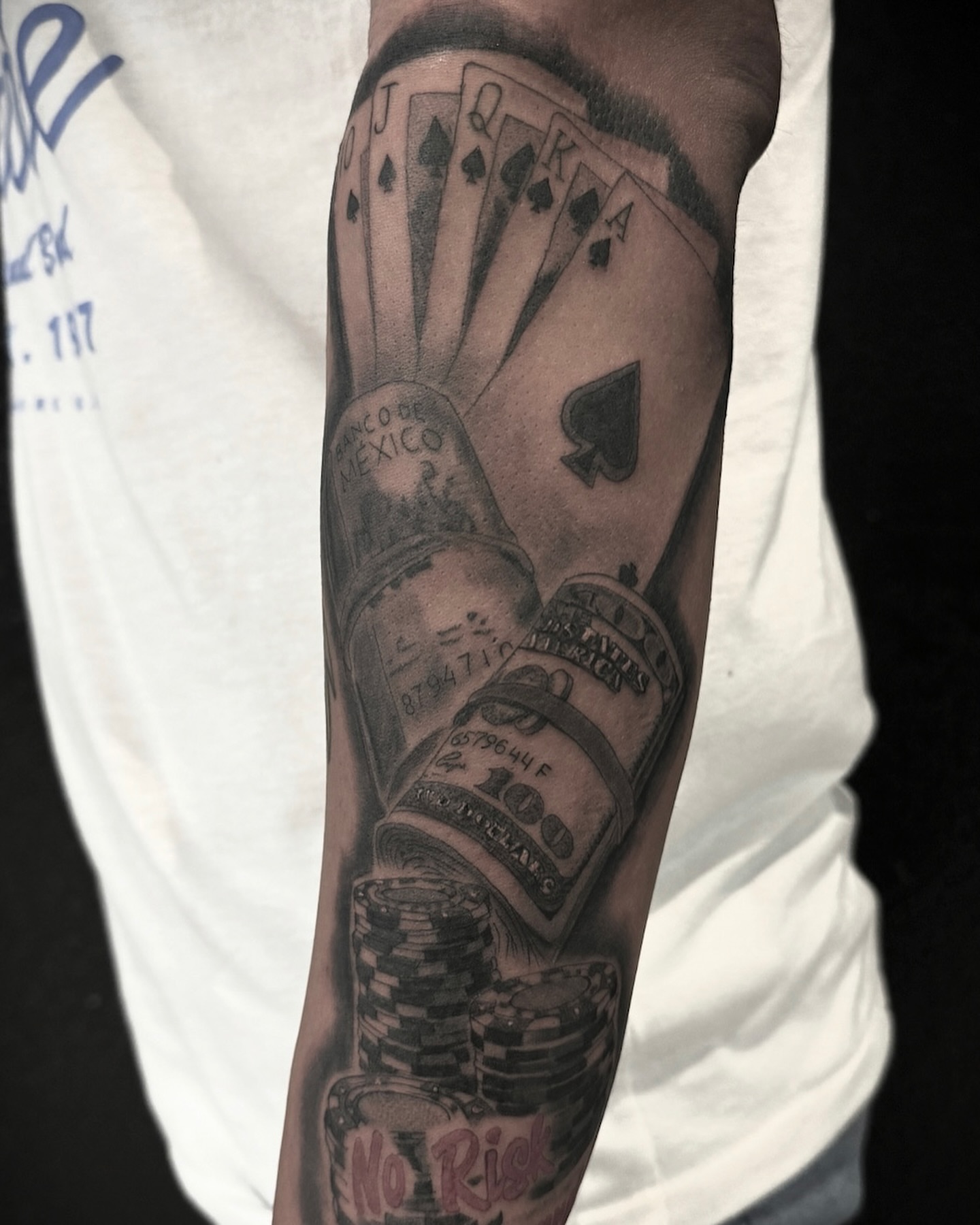 Playing cards and money black and grey tattoo on the forearm by Chip