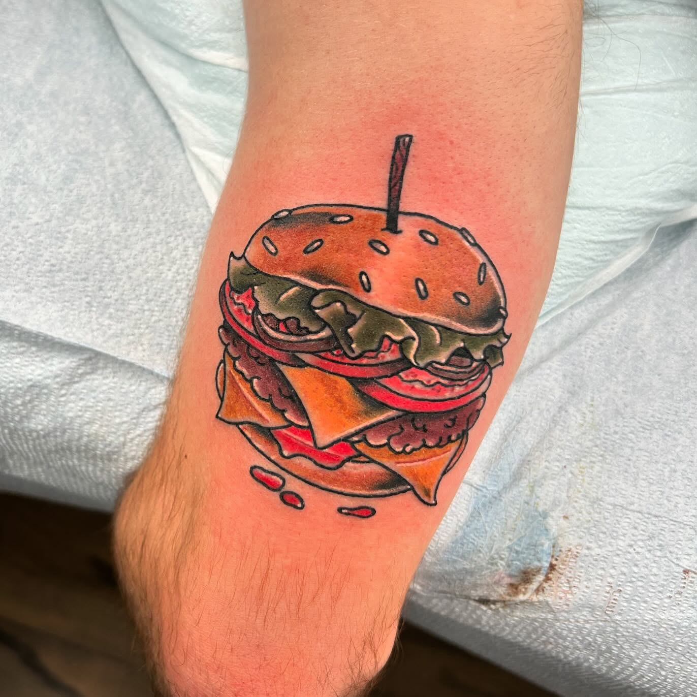Hamburger realism tattoo on the forearm by Noah Crow
