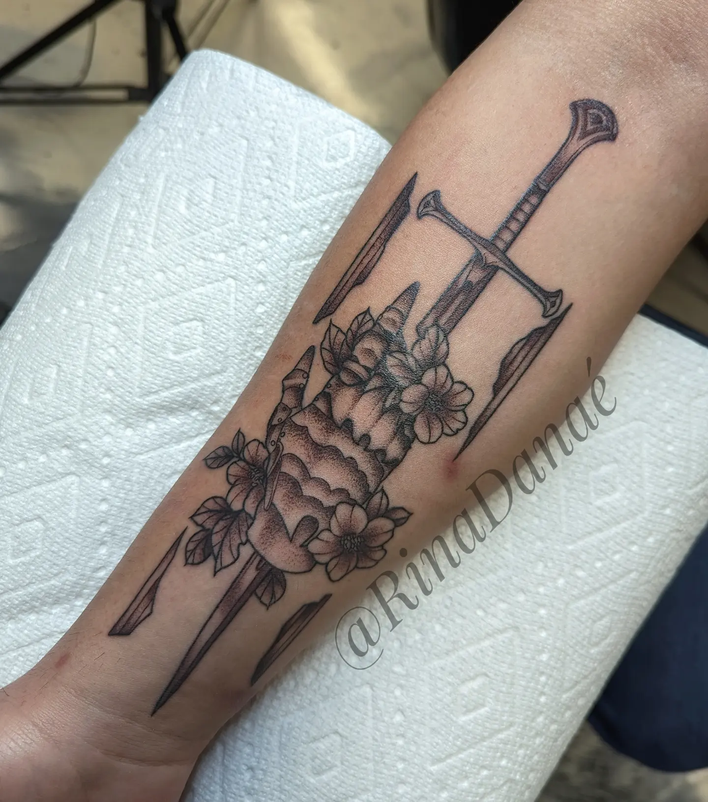 Crossed swords and skull black and grey tattoo on the forearm by Rina Danaé Tattoo🌿