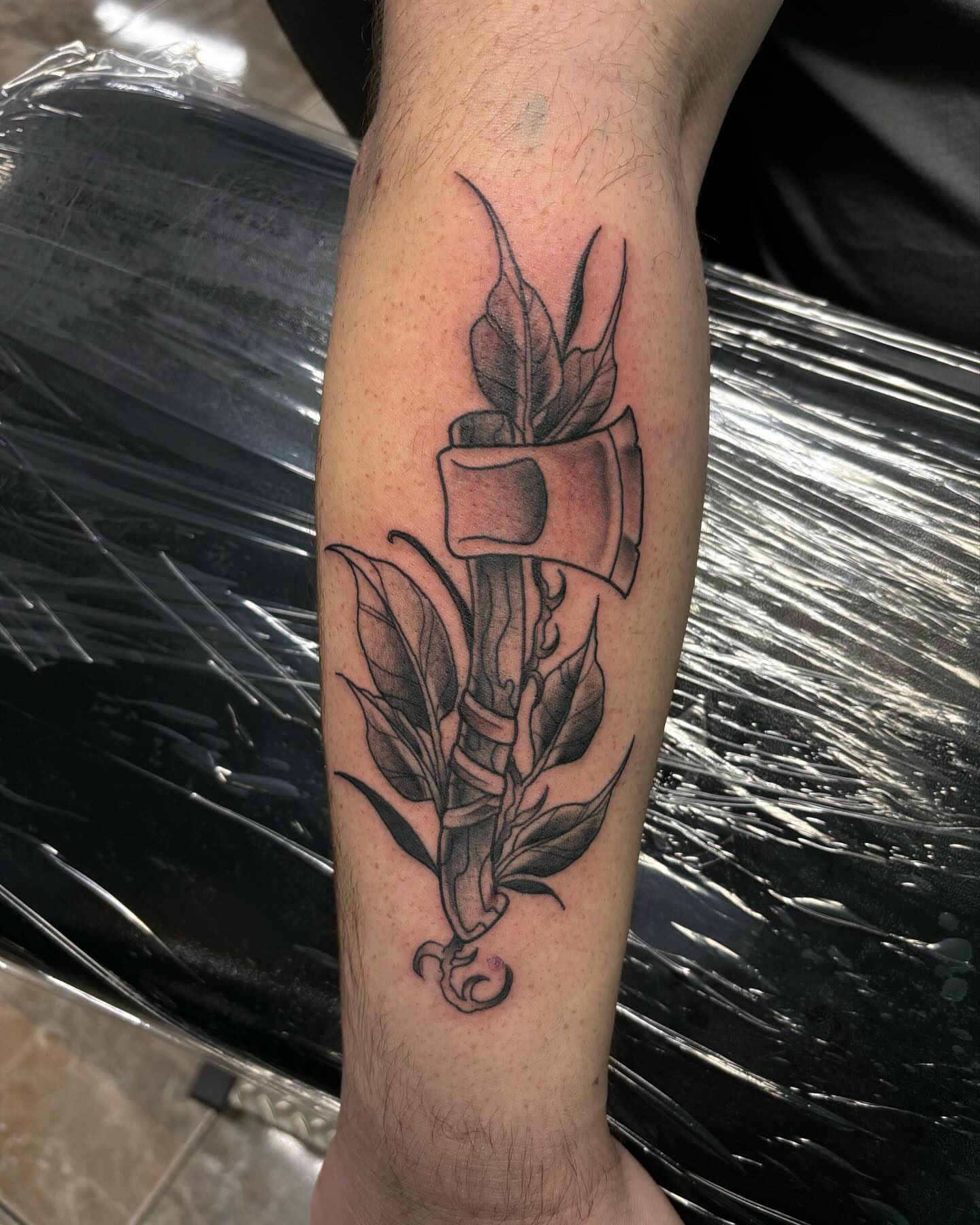 Axe and leaves black and grey tattoo on the forearm by Ares Rhodes