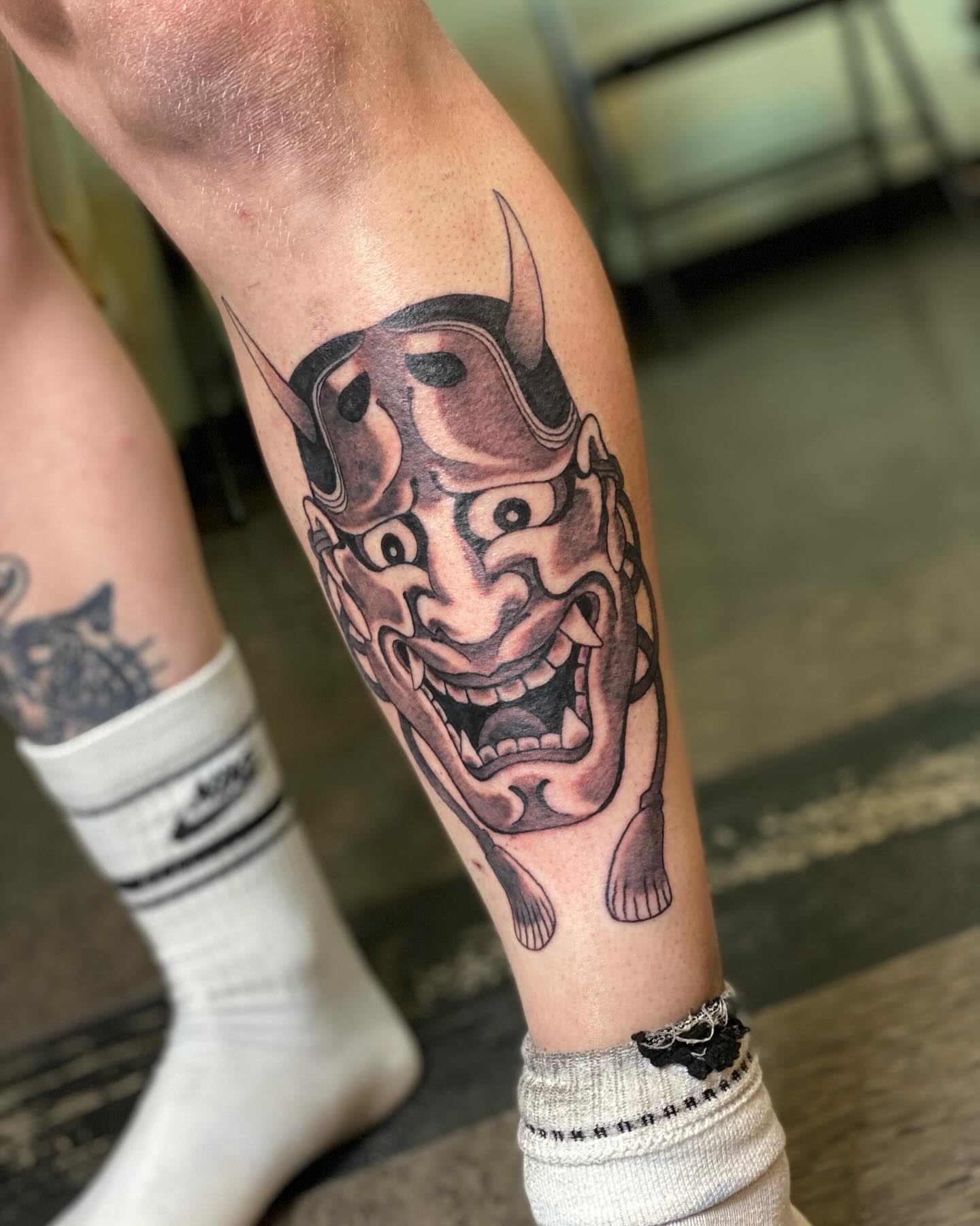 Demon mask black and grey tattoo on the forearm by Hayden Earley