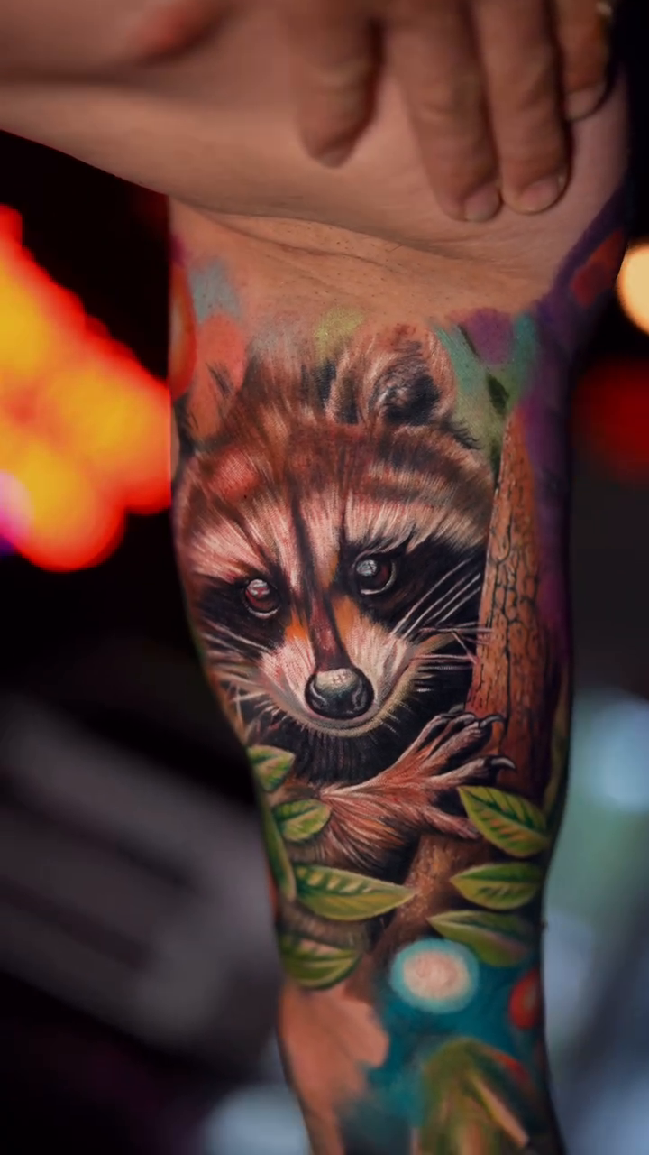 Raccoon in a forest setting realism tattoo by Yasmani ramirez
