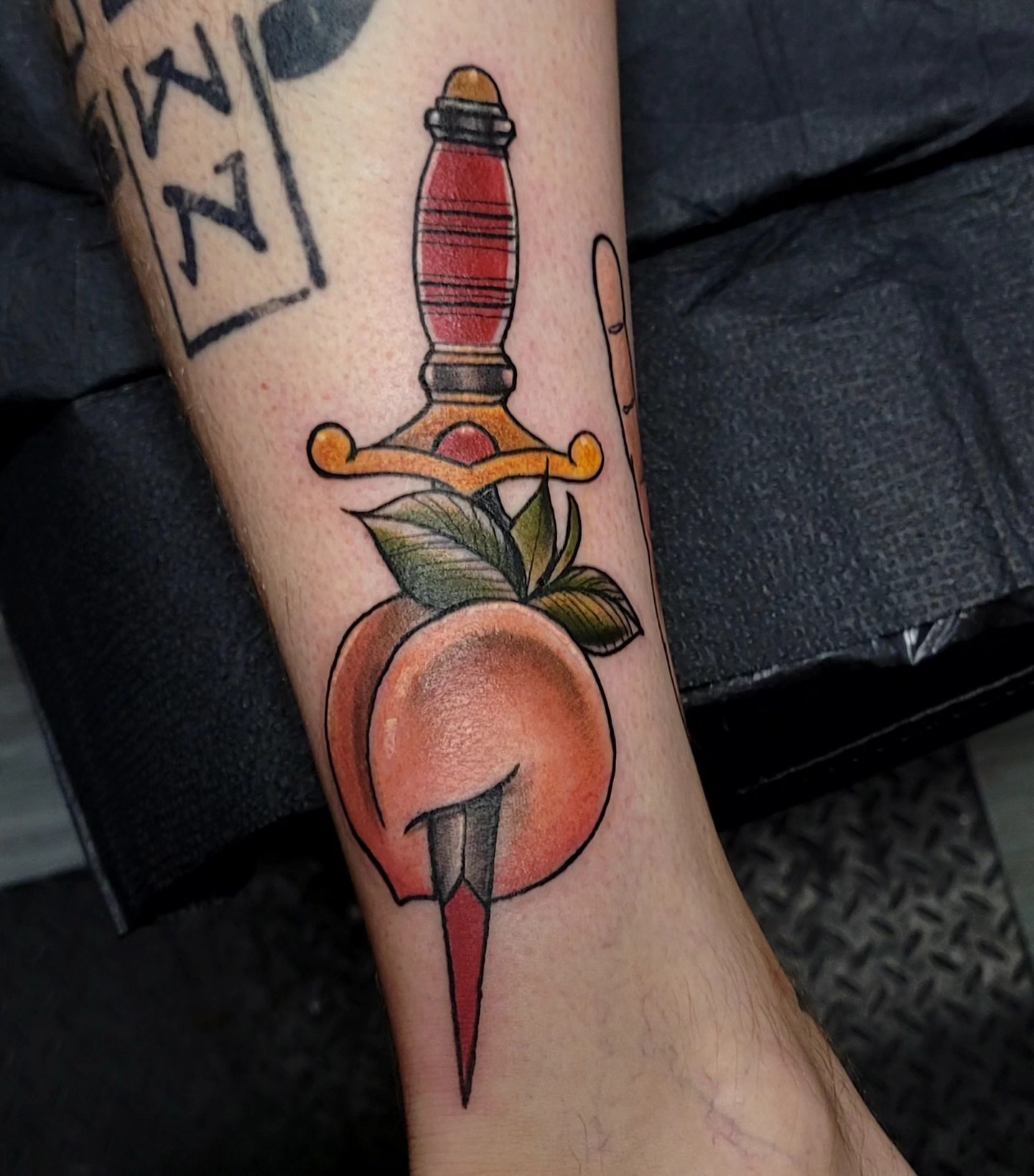 Peach and dagger American traditional tattoo on the forearm by Dawne Michele