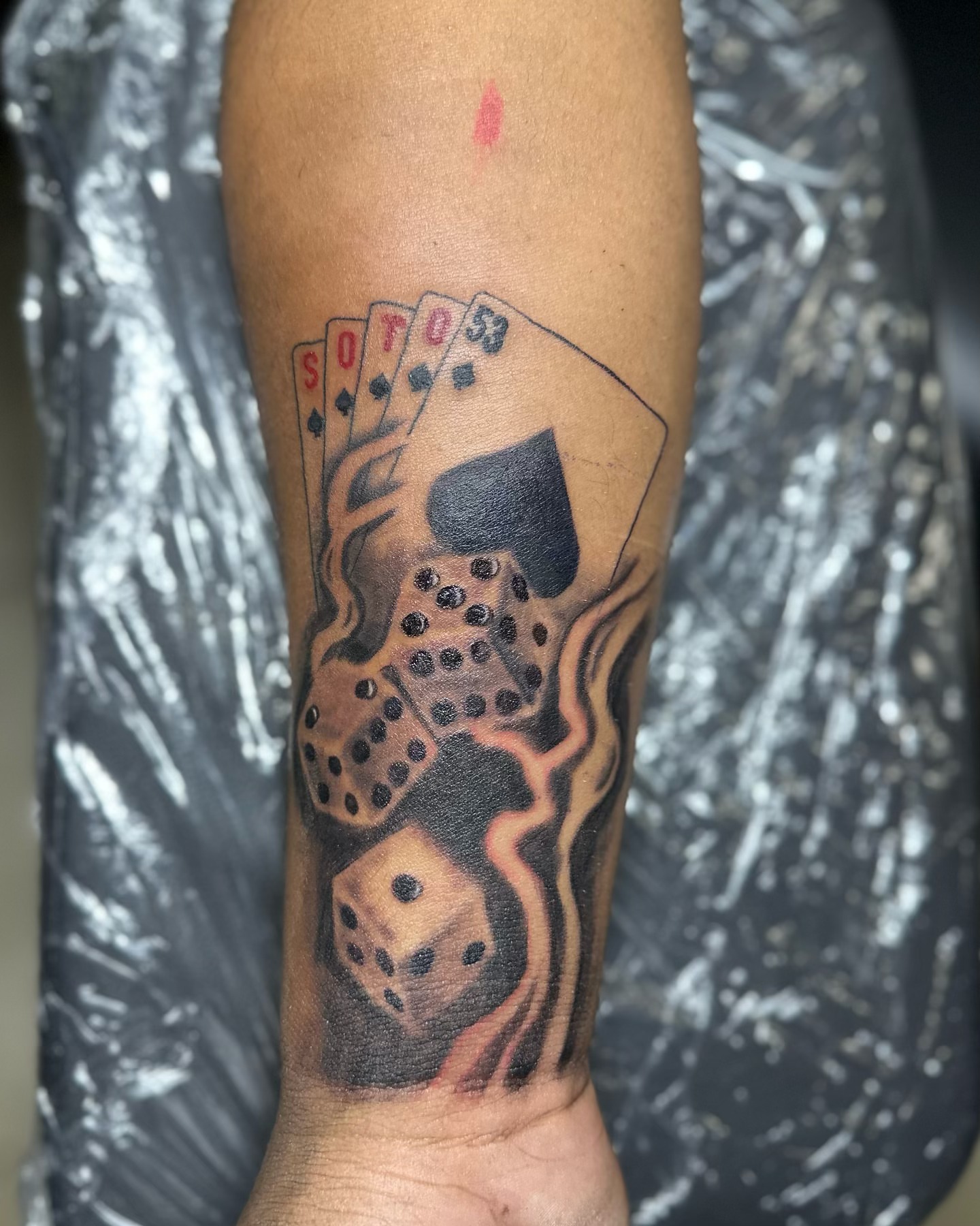 Playing cards and dice black and grey tattoo on the forearm by Devin