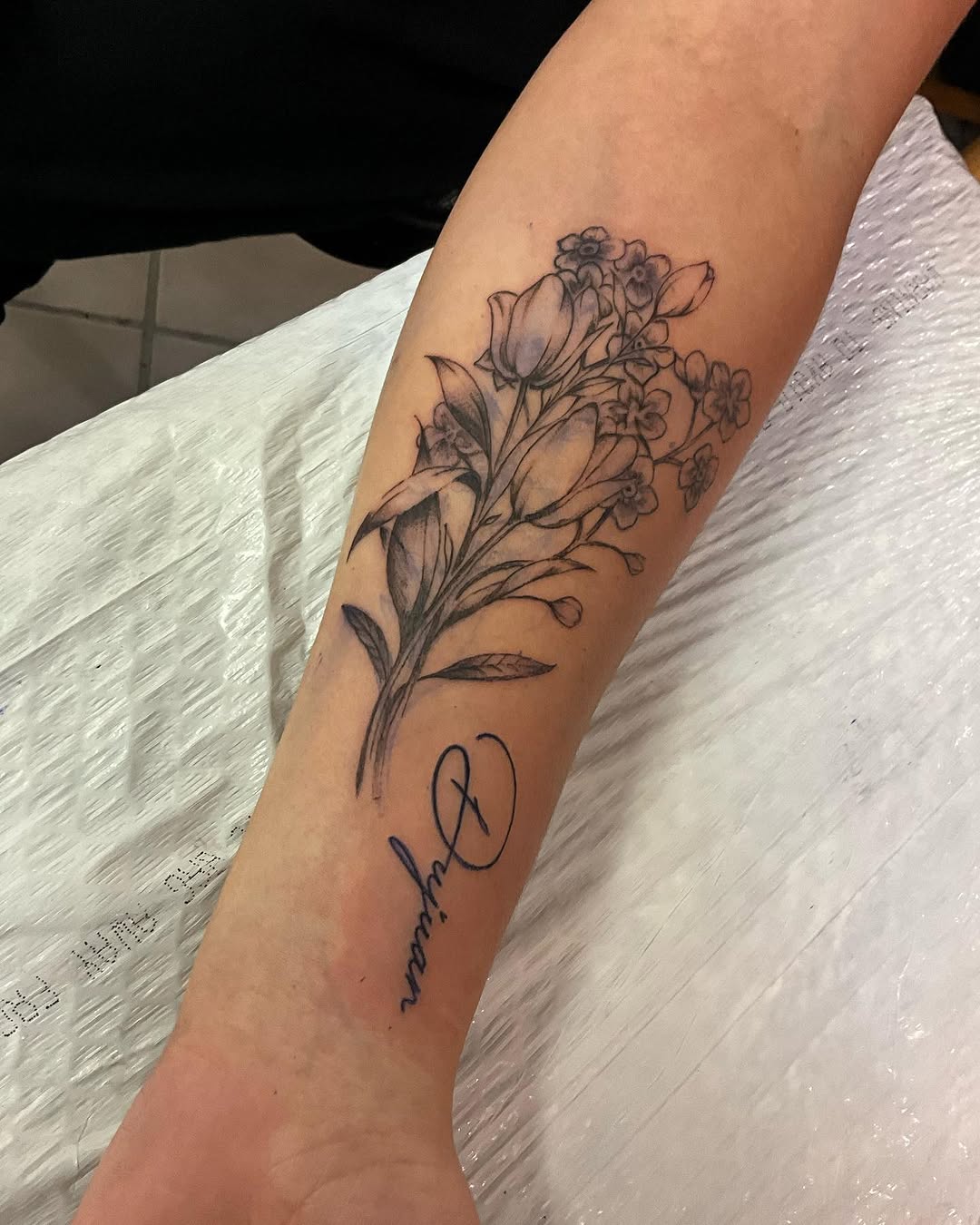 Bouquet of flowers and script name fine line tattoo on the forearm by Bear