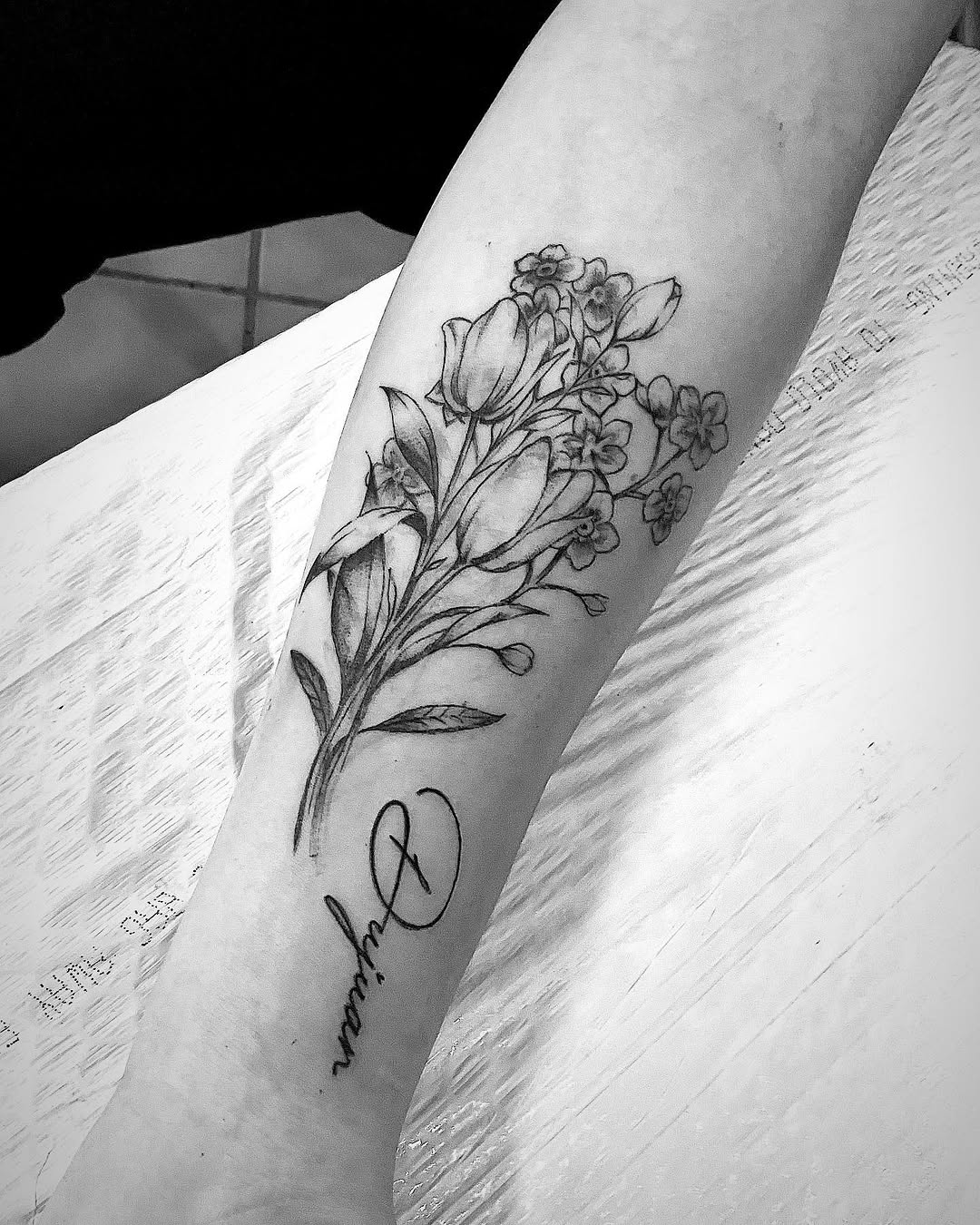 Floral bouquet with script name tattoo on the forearm by Bear