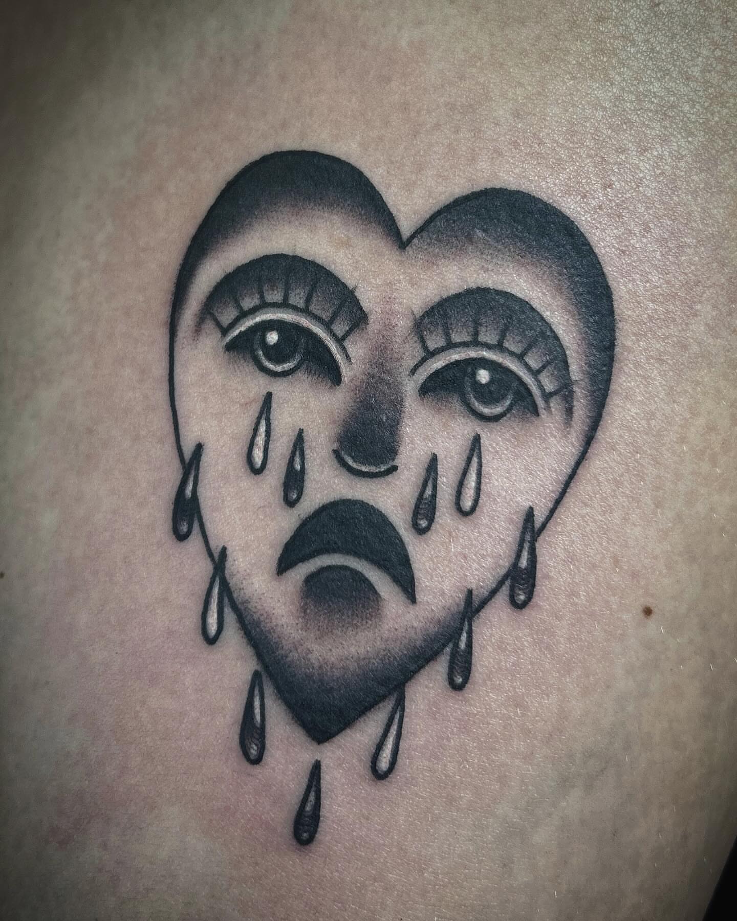 Heart with crying face black and grey tattoo on the shoulder by Samantha C, Bremerton, Washington