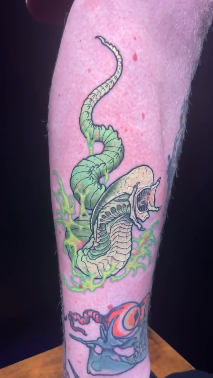 Alien xenomorph with snake-like tail American traditional tattoo on the upper arm by Joe Moreira
