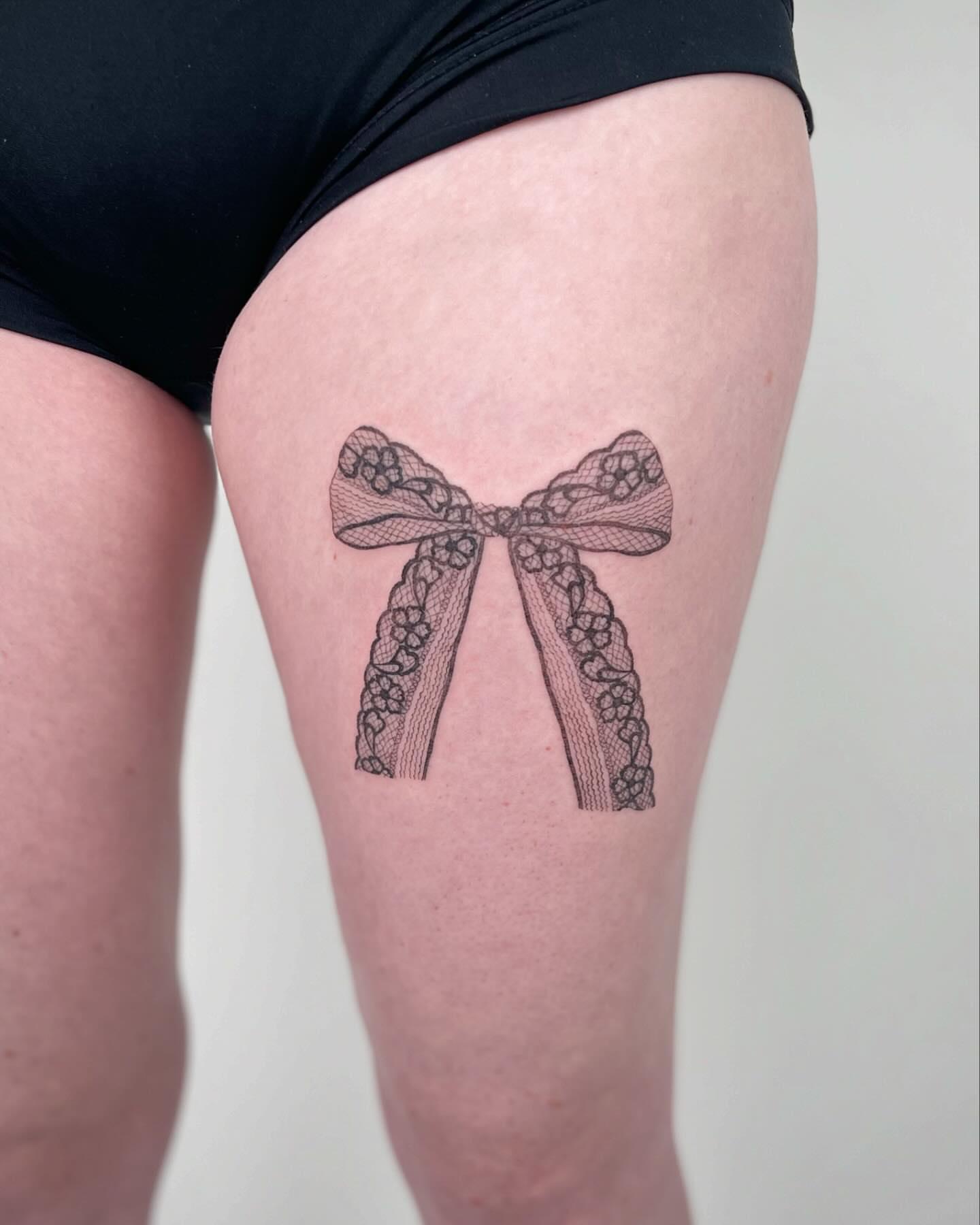Bow black and grey tattoo on the thigh by Jennifer Fuster