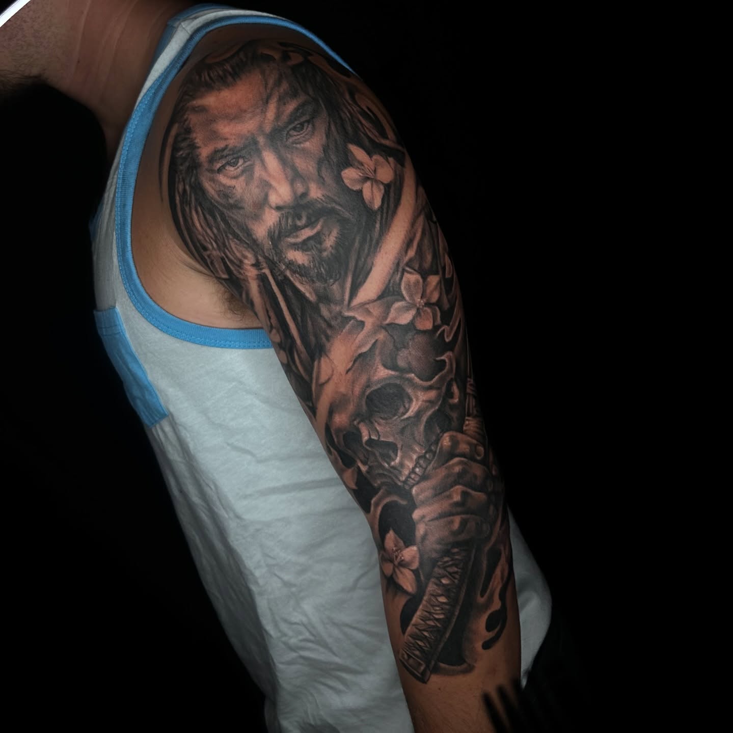 Man with flowers and skull realism tattoo on the upper arm by Alia