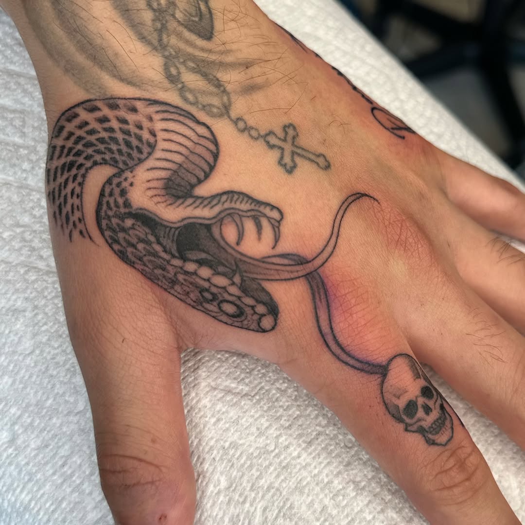 Snake with skull and cross American traditional tattoo on the hand by Allison Vargas