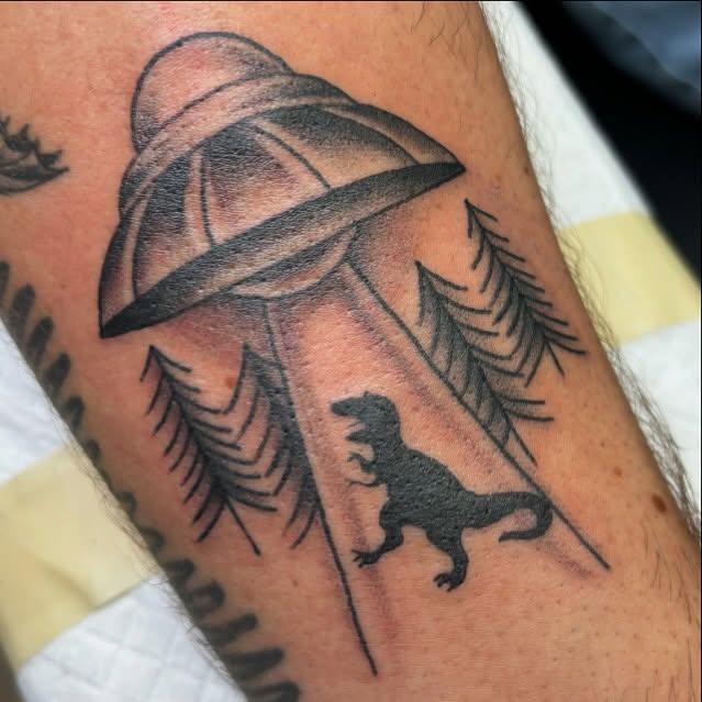 Dinosaur and UFO realism tattoo on the forearm by Amy Kolton