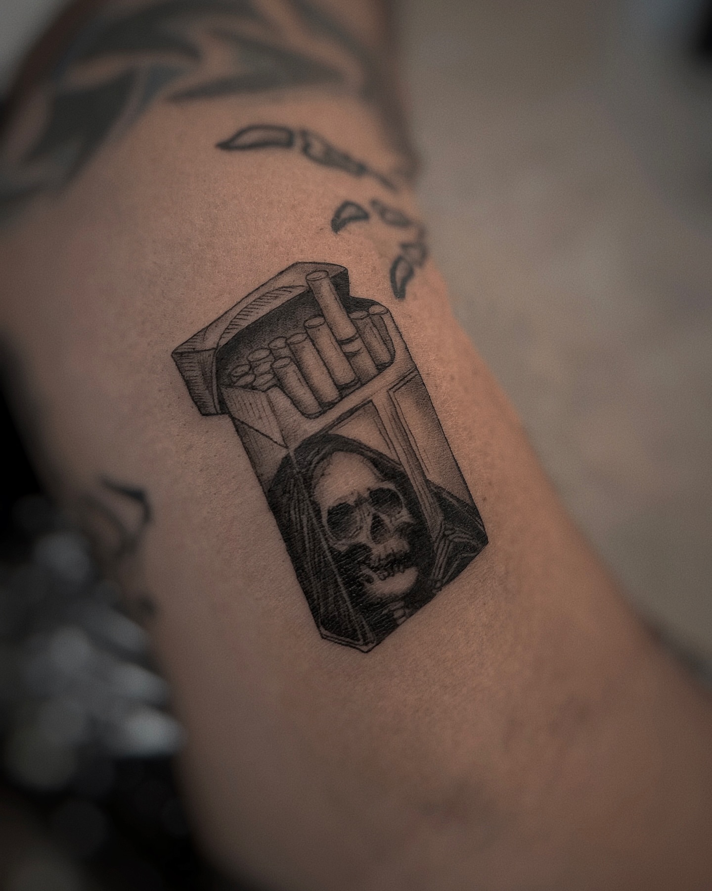 Cigarette pack with skull realism tattoo on the forearm by Lily K.