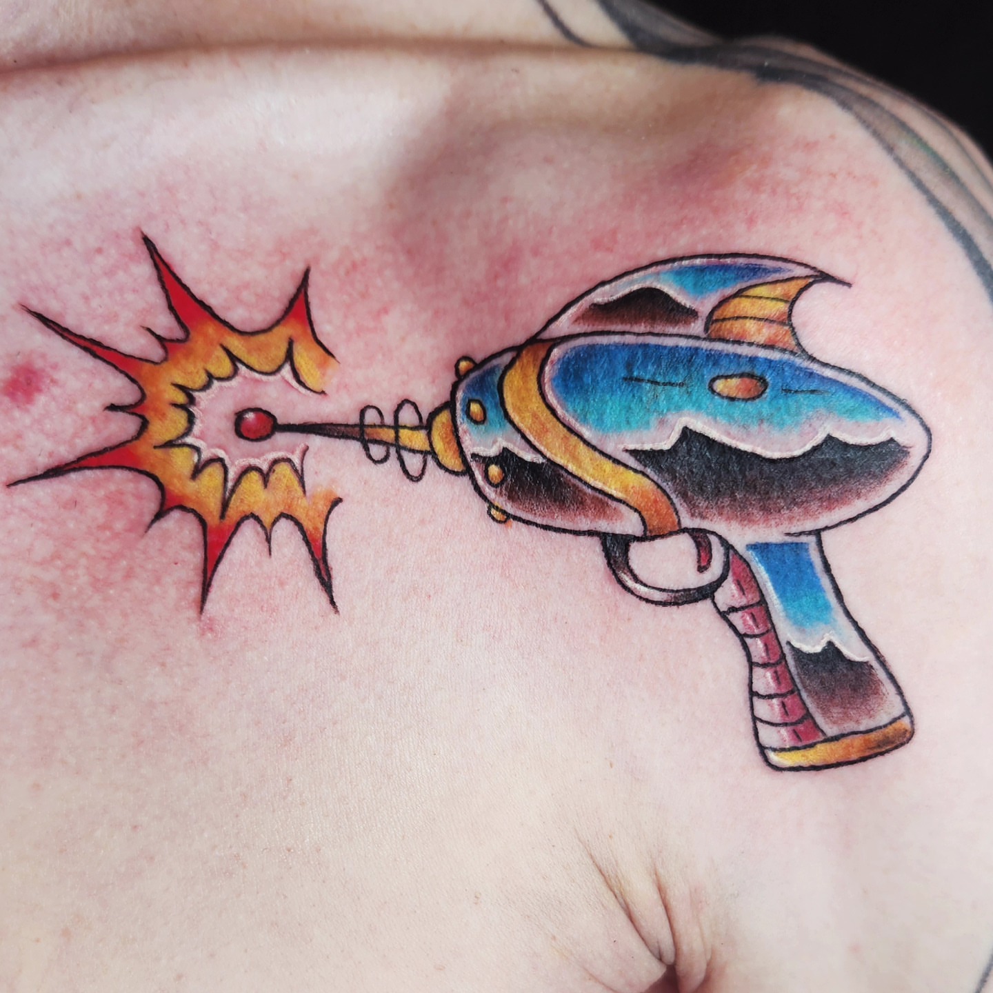 Gun with explosion new school tattoo on the shoulder by Audrey Luther