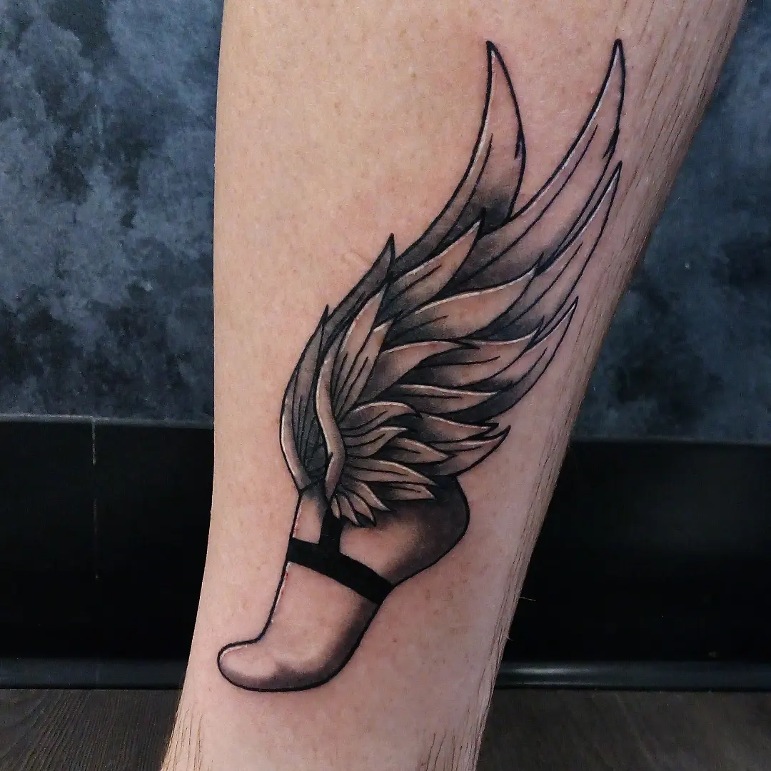 Winged ballet shoe black and grey tattoo on the calf by Cassandra Davis
