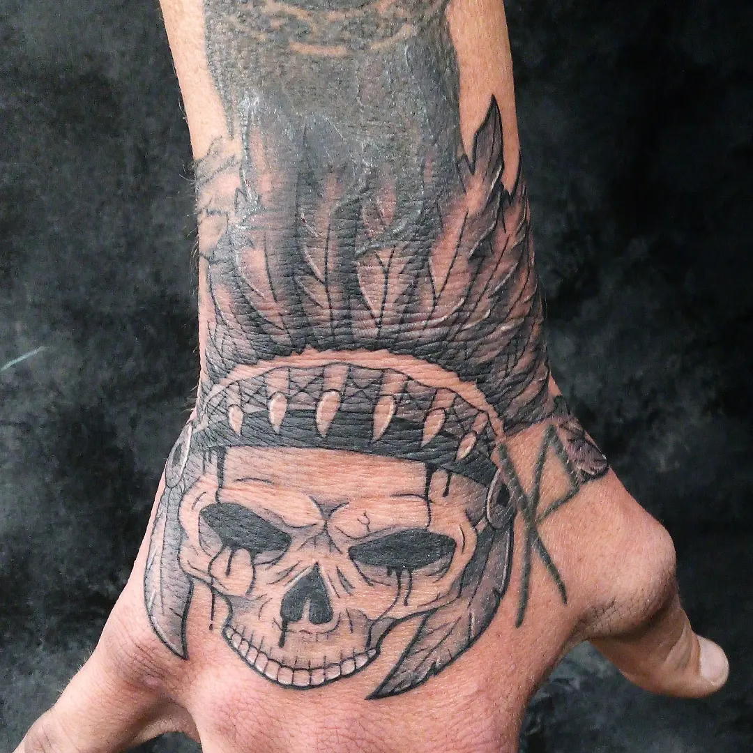 Skull with feathers realism tattoo on the hand by Cassandra Davis