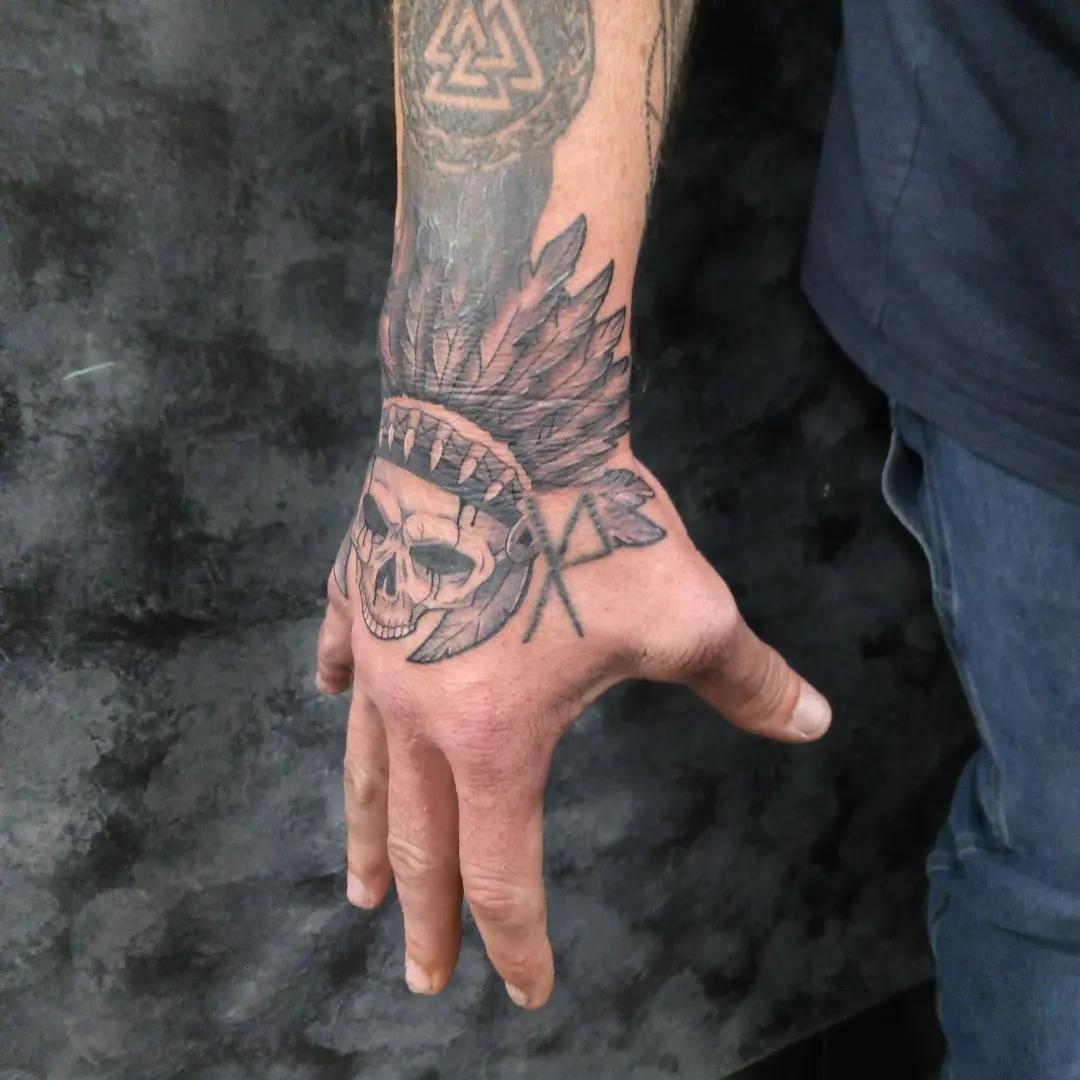 Skull with feathers realism tattoo on the hand by Cassandra Davis