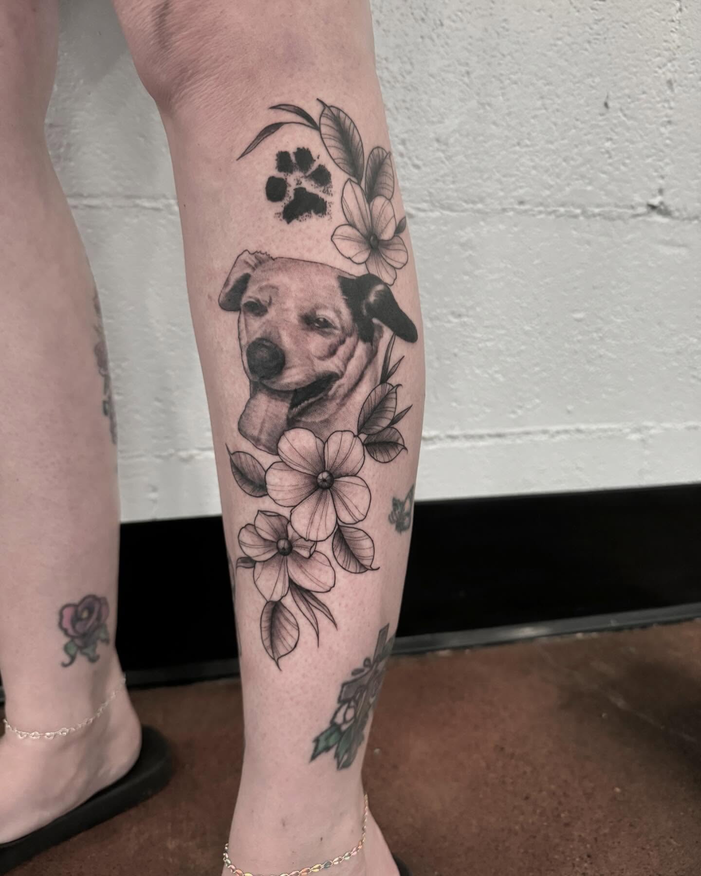 Dog with flowers black and grey tattoo on the calf by Drew Foster, Toledo, Ohio