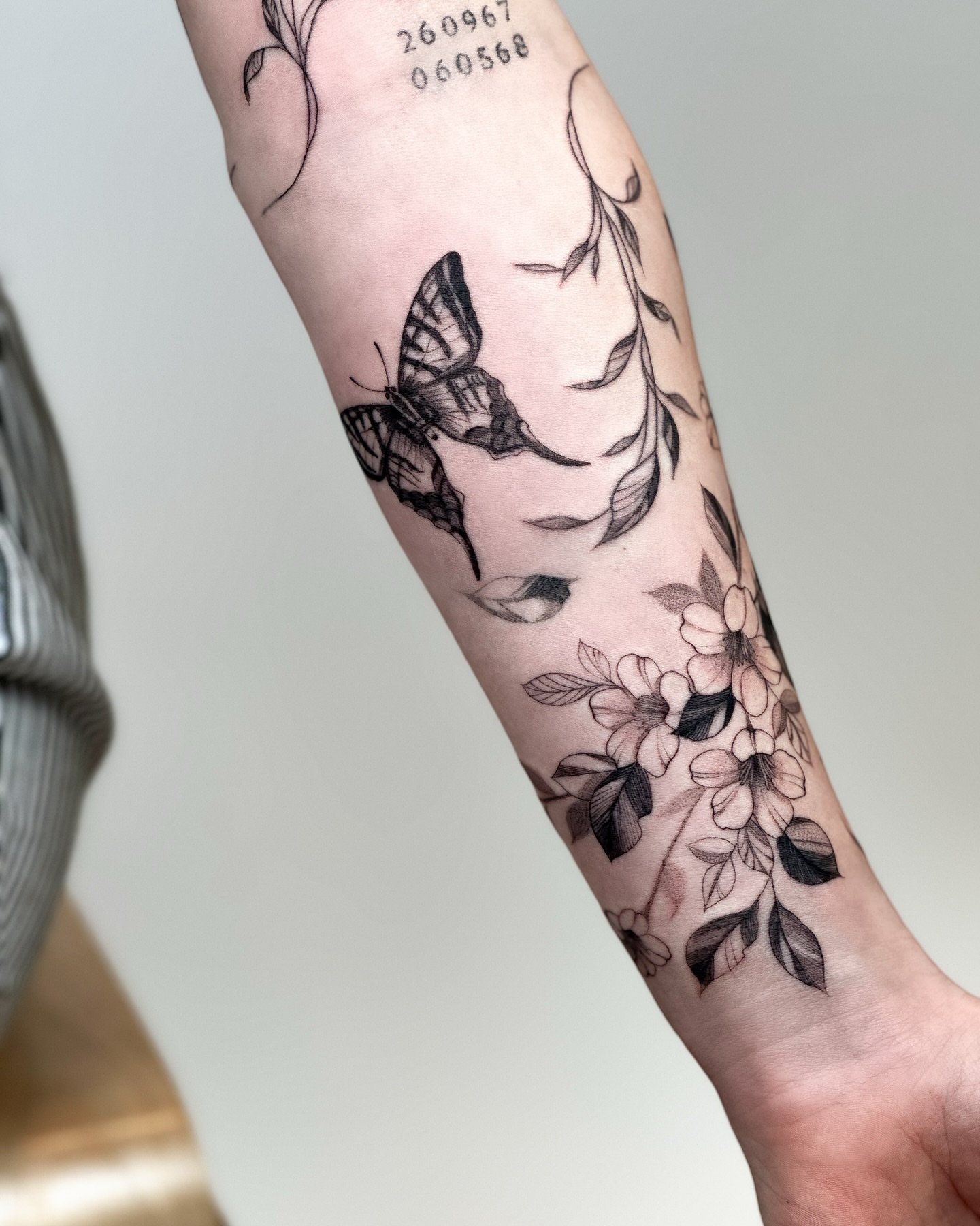 Butterfly and flowers black and grey tattoo on the forearm by Liv