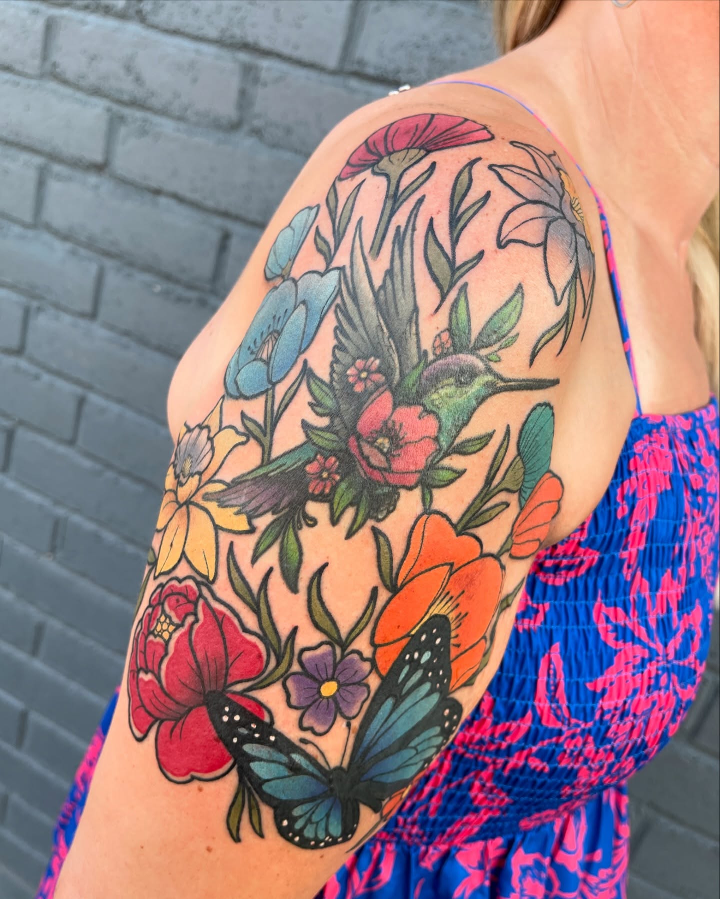 Floral arrangement with hummingbird American traditional tattoo on the upper arm by Chris Sparks, I just go by Sparks.