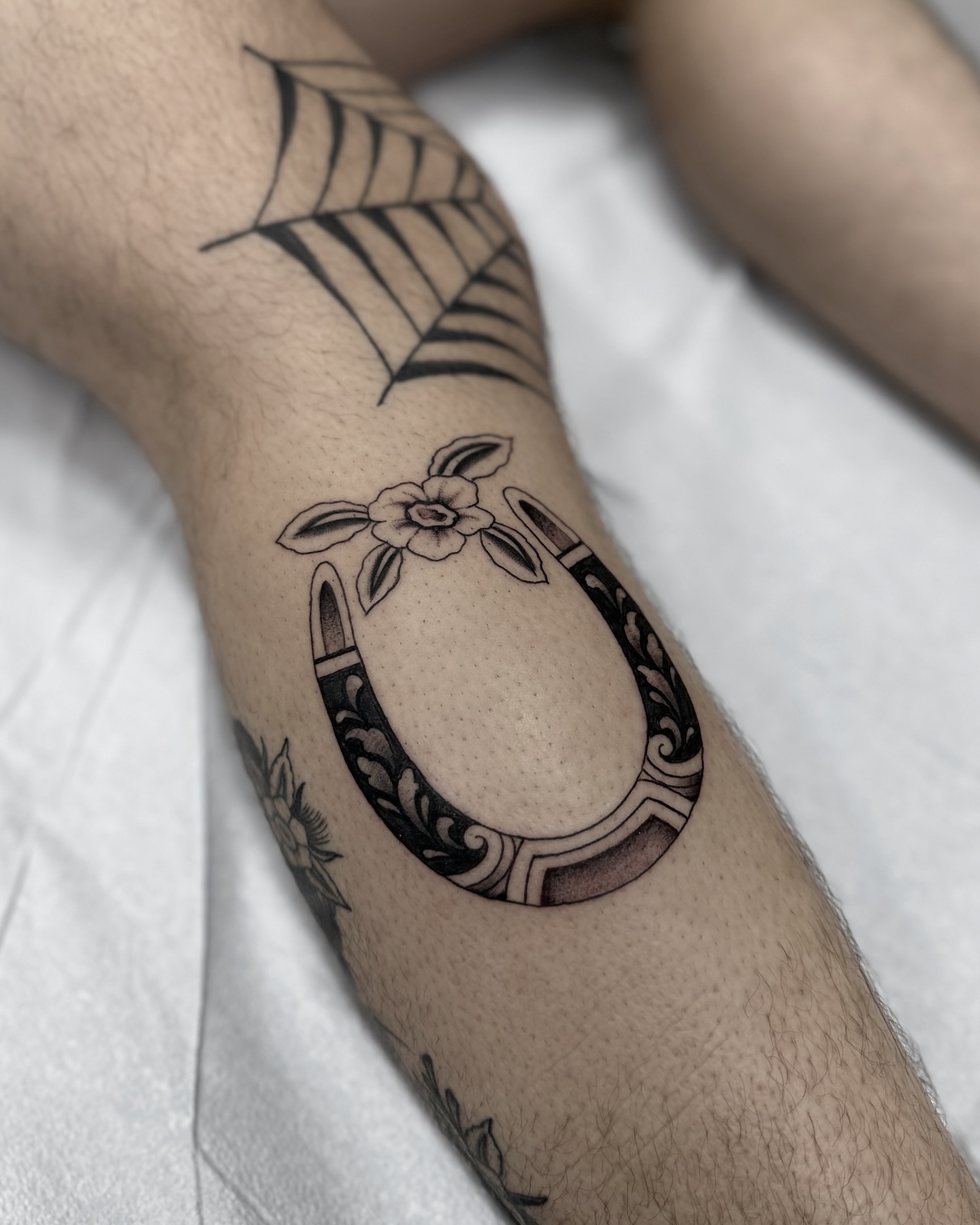 Horseshoe with floral decoration black and grey tattoo on the forearm by Nicholas Lee, San Francisco, California