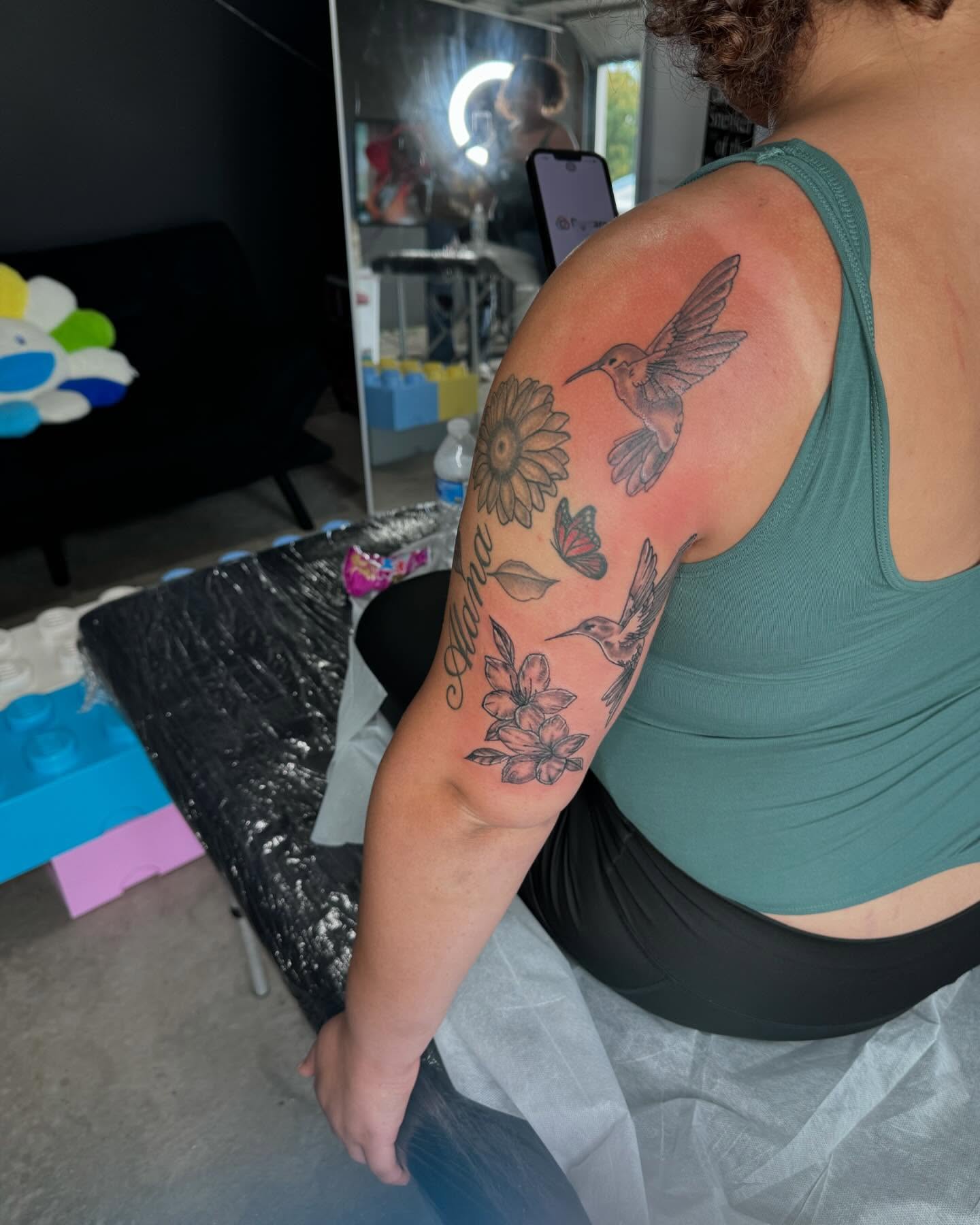 Hummingbird and flowers new school tattoo on the upper arm by Sierra 🩷