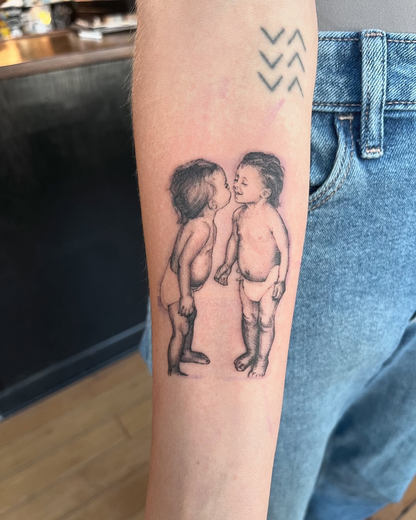 Two babies kissing realism tattoo on the forearm by Sarah Spread
