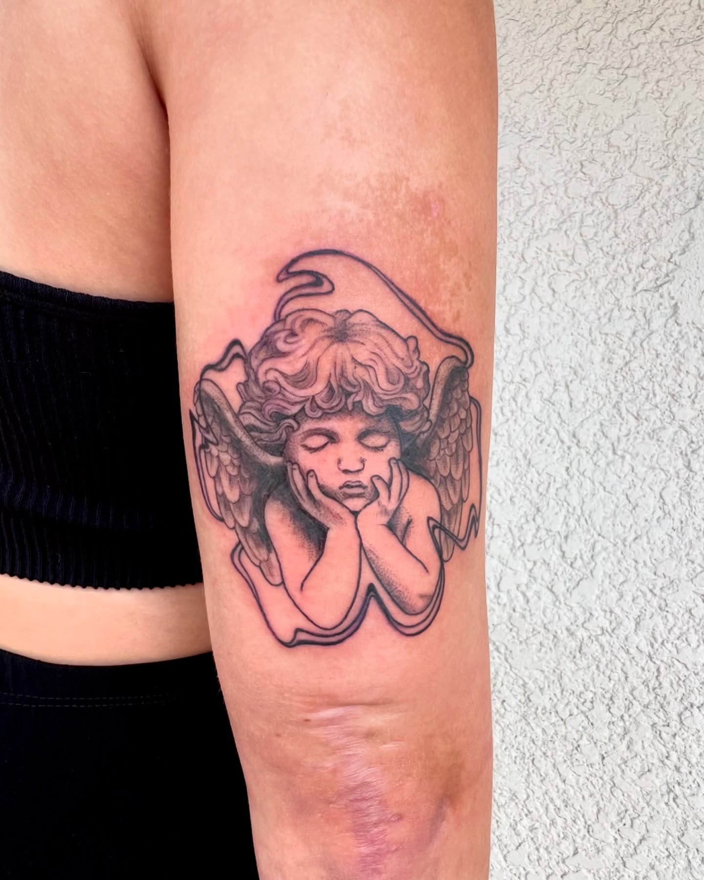 Cherub black and grey tattoo on the forearm by Maddy Paige