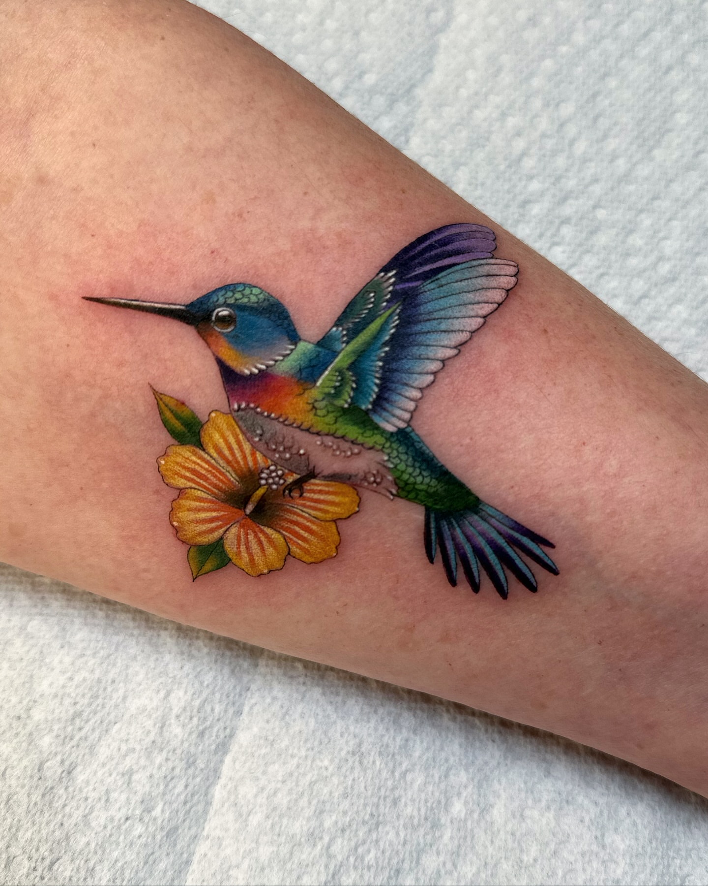 Hummingbird and flower realism tattoo on the forearm by Savannah Compton