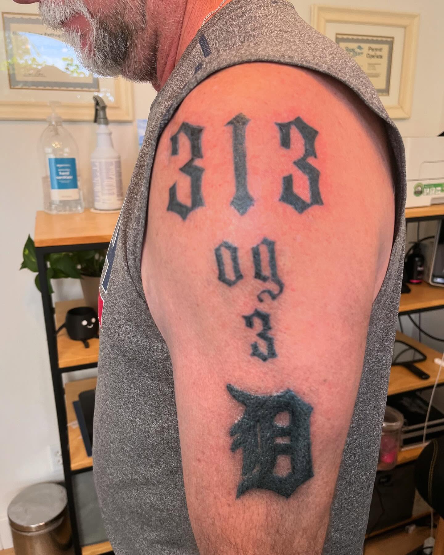 Numbers and Detroit logo black and grey tattoo on the shoulder by Val Maughan