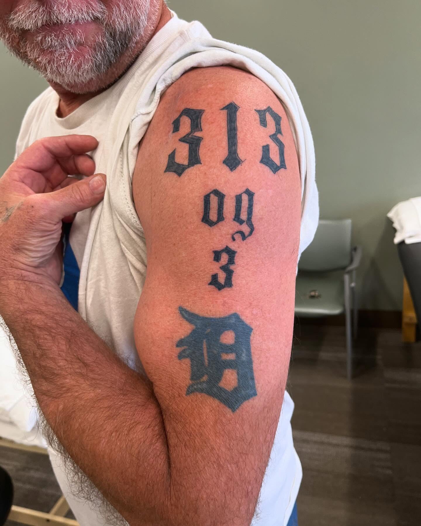 Numbers and Detroit Tigers logo lettering script tattoo on the upper arm by Val Maughan