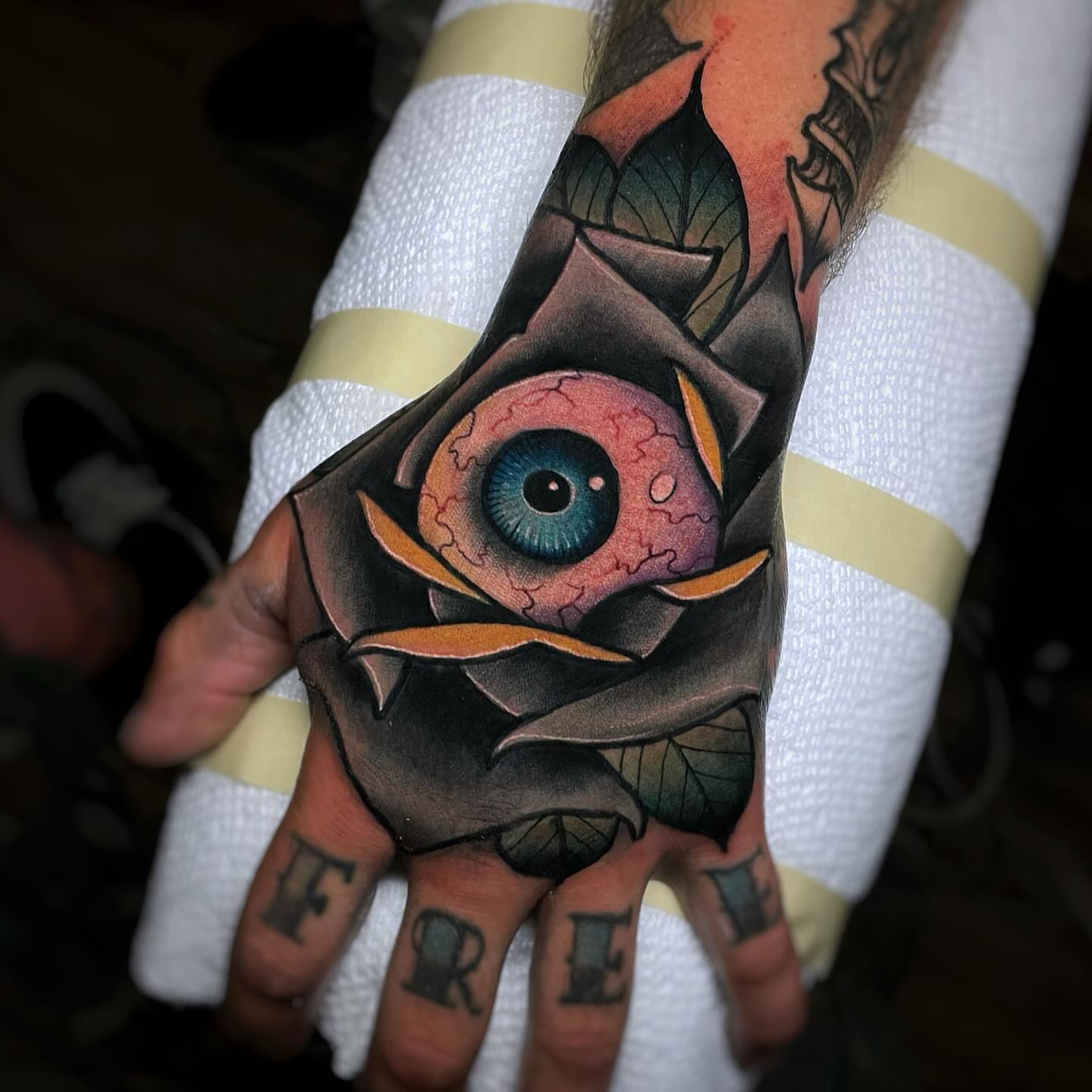Eye within rose American traditional tattoo on the hand by Ick Abrams